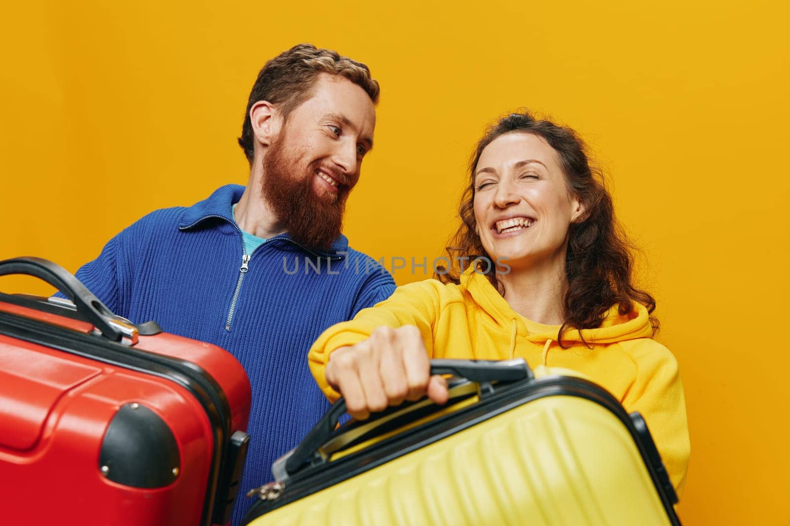 Woman and man smiling, suitcases in hand with yellow and red suitcase smiling merrily and crooked, yellow background, going on a trip, family vacation trip, newlyweds. High quality photo