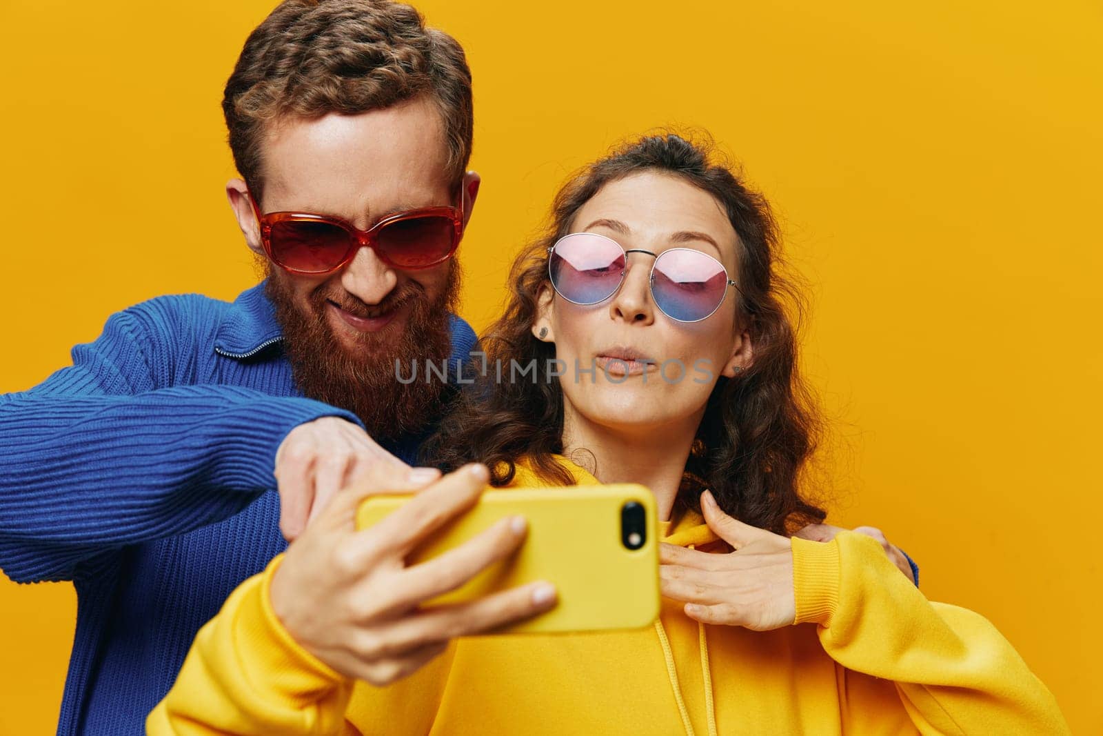 Woman and man funny couple with phones in hand social networking and communication crooked do selfies smile fun, on yellow background. The concept of real family relationships, freelancers, work online. High quality photo