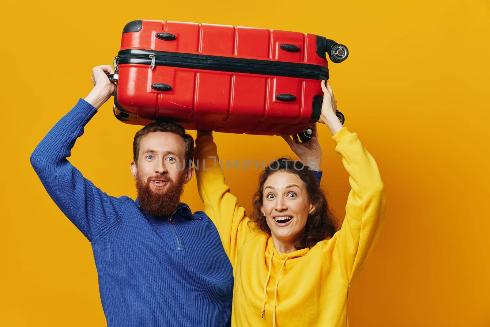 Woman and man smiling, suitcases in hand with yellow and red suitcase smiling merrily and crooked, yellow background, going on a trip, family vacation trip, newlyweds. High quality photo