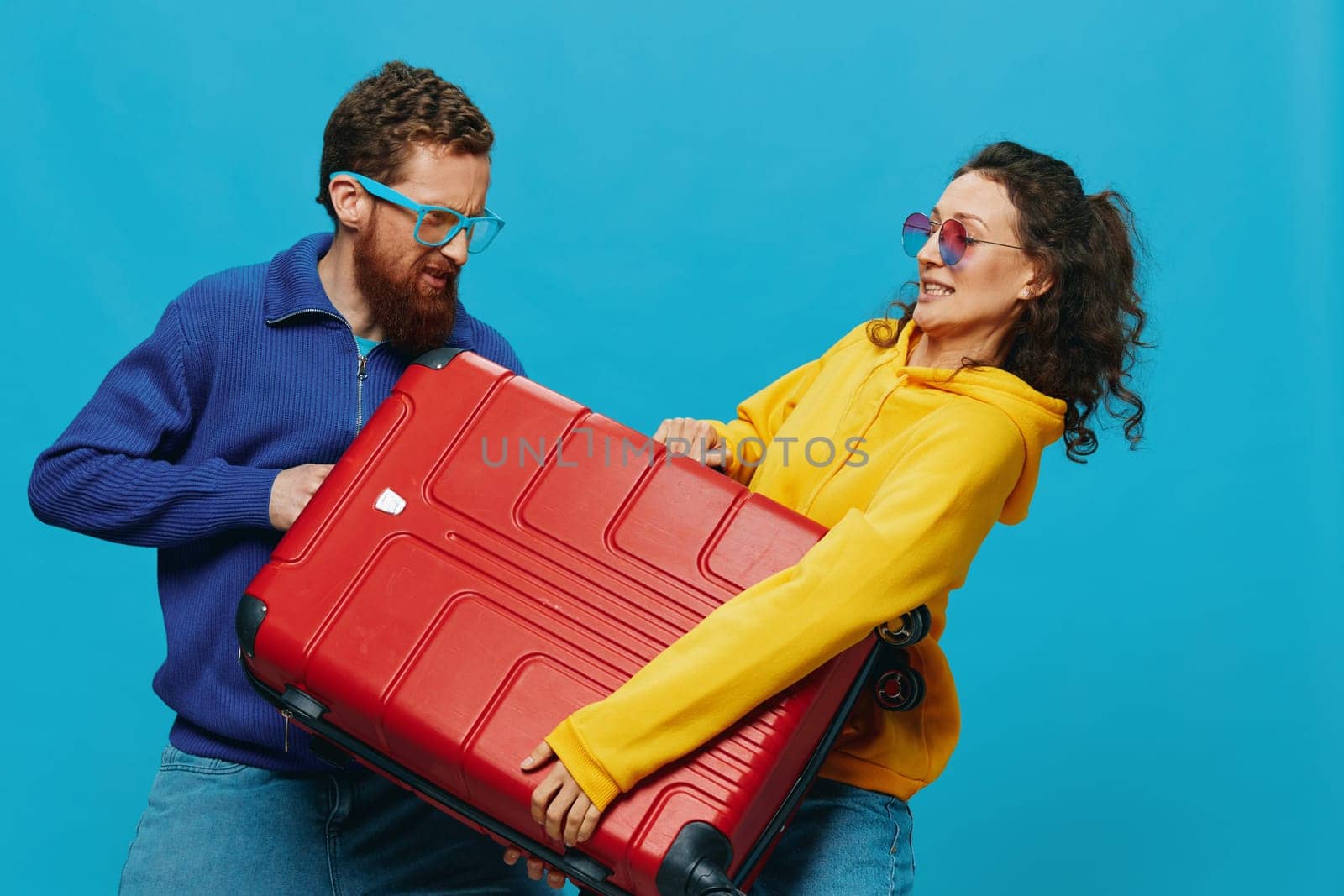 Woman and man smile suitcases in hand with yellow and red suitcase smile fun, on blue background, packing for a trip, family vacation trip. by SHOTPRIME