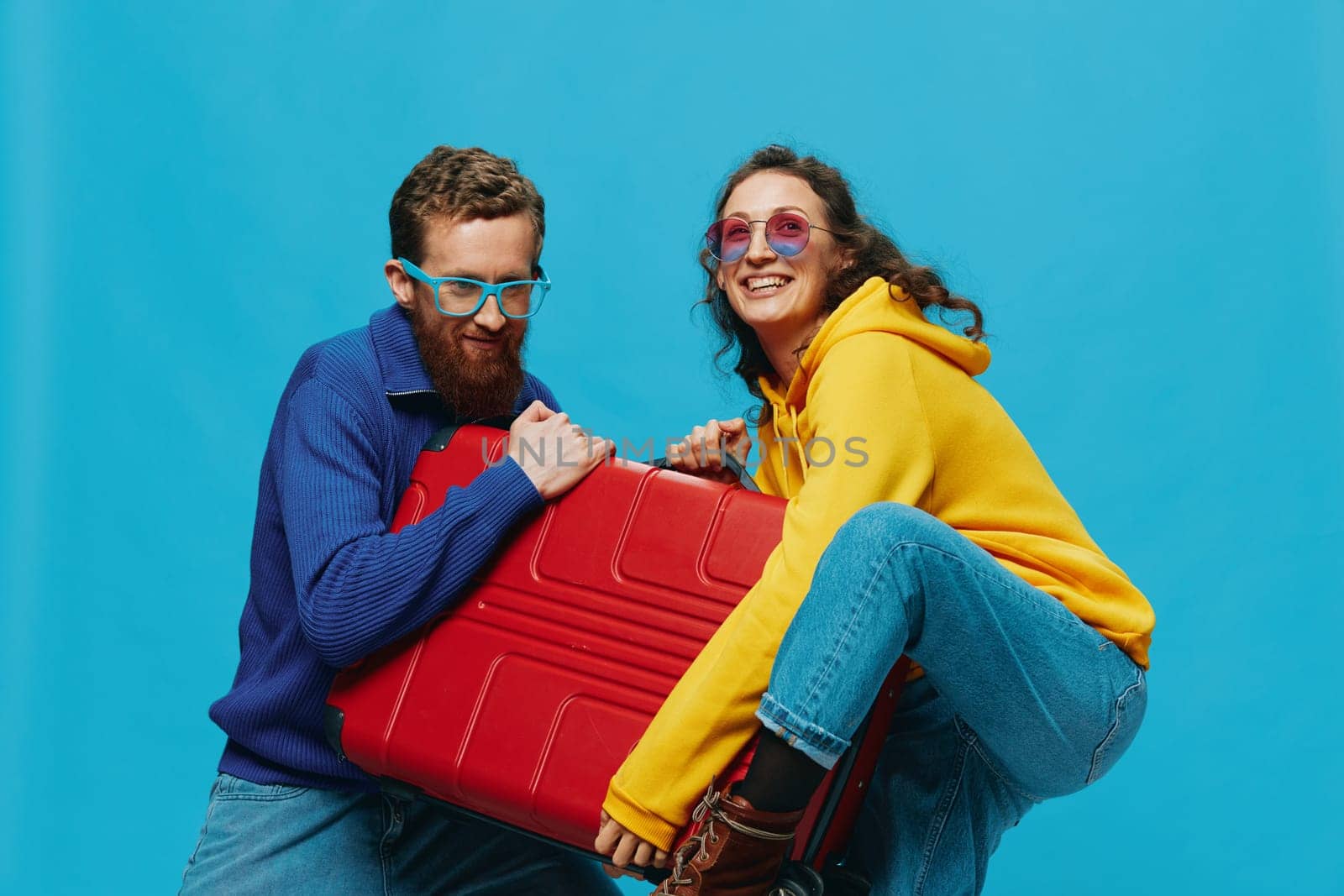 Woman and man smile suitcases in hand with yellow and red suitcase smile fun, on blue background, packing for a trip, family vacation trip. by SHOTPRIME