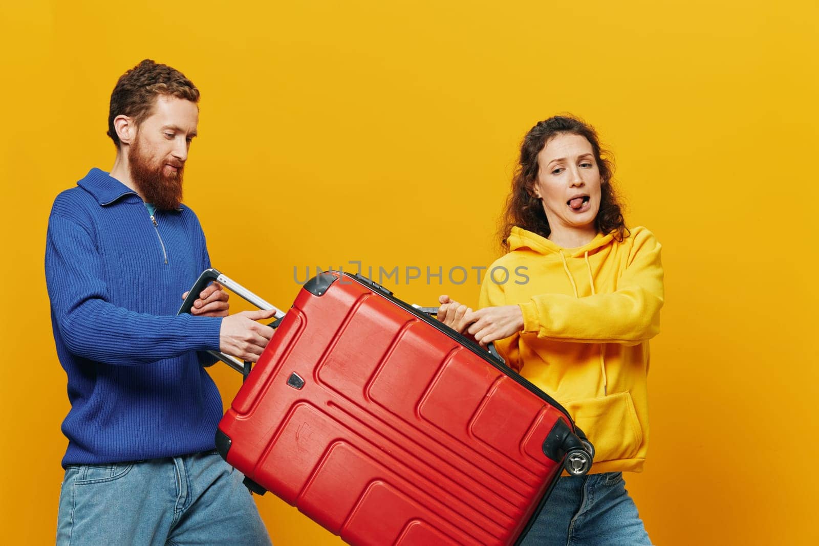 Woman and man smiling, suitcases in hand with yellow and red suitcase smiling merrily and crooked, yellow background, going on a trip, family vacation trip, newlyweds. by SHOTPRIME