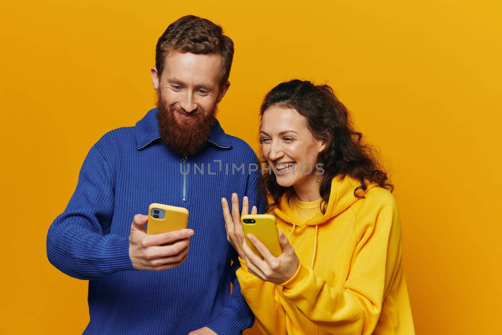 Man and woman couple smiling merrily with phone in hand social media viewing photos and videos, on yellow background, symbols signs and hand gestures, family freelancers. by SHOTPRIME