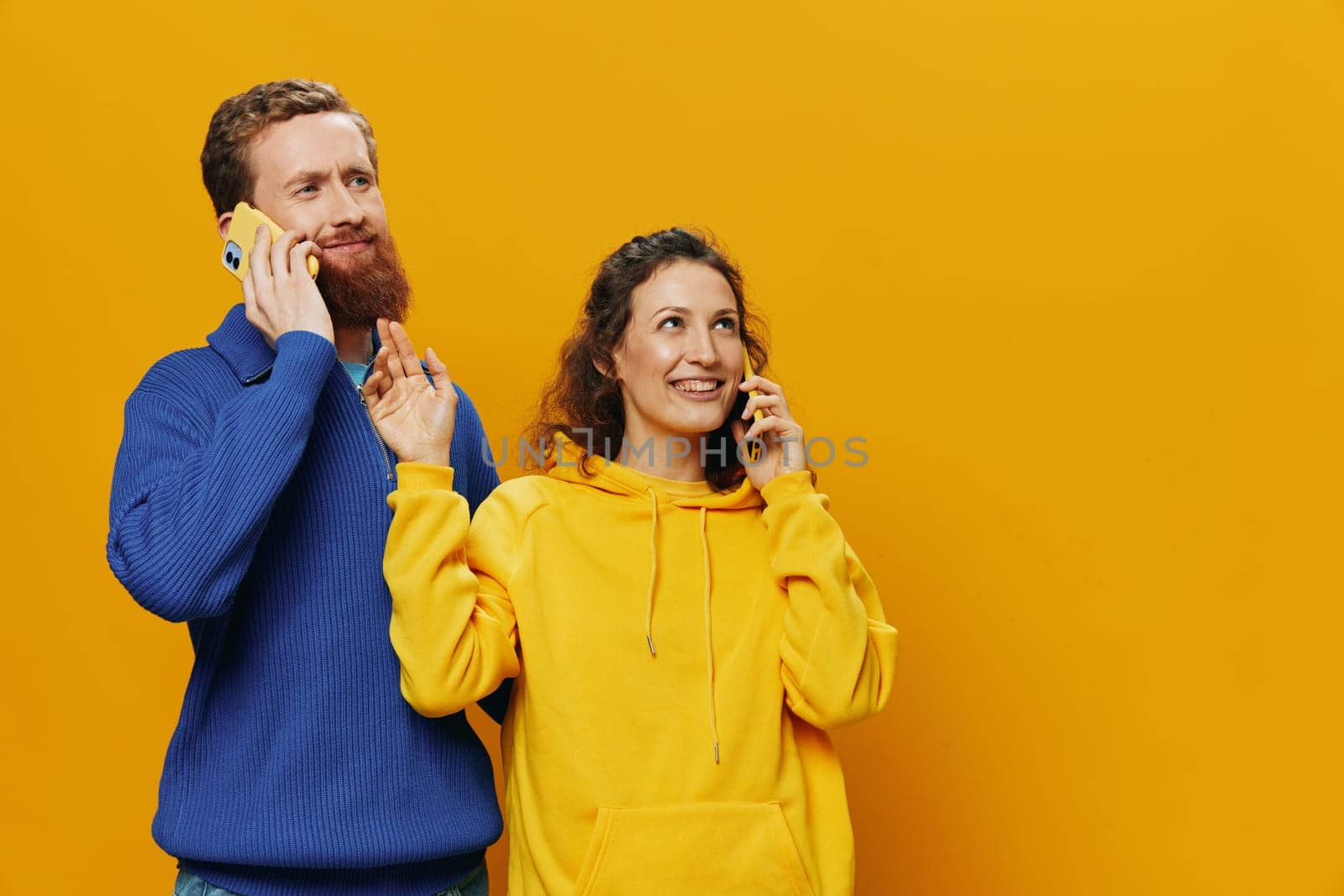 Woman and man cheerful couple with phones in hand talking on cell phone crooked smile cheerful, on yellow background. The concept of real family relationships, talking on the phone, work online. High quality photo