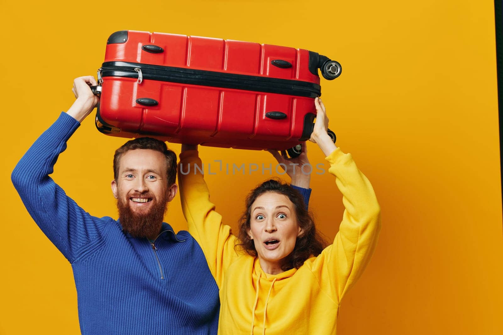 Woman and man smiling, suitcases in hand with yellow and red suitcase smiling merrily and crooked, yellow background, going on a trip, family vacation trip, newlyweds. by SHOTPRIME