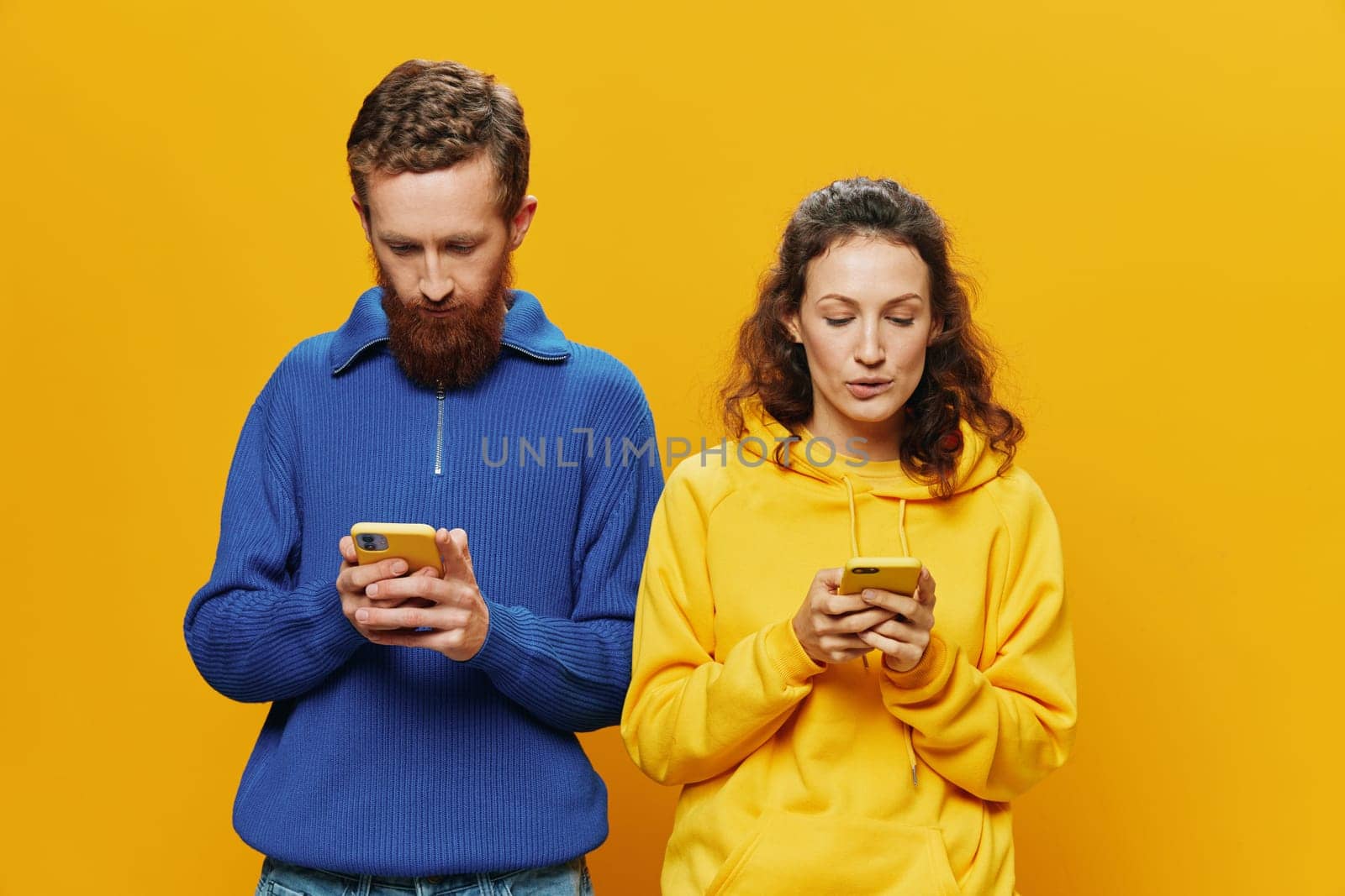 Woman and man cheerful couple with phones in hand social networking and communication crooked smile fun and fight, in yellow background. The concept of real family relationships, freelancers, work online. High quality photo