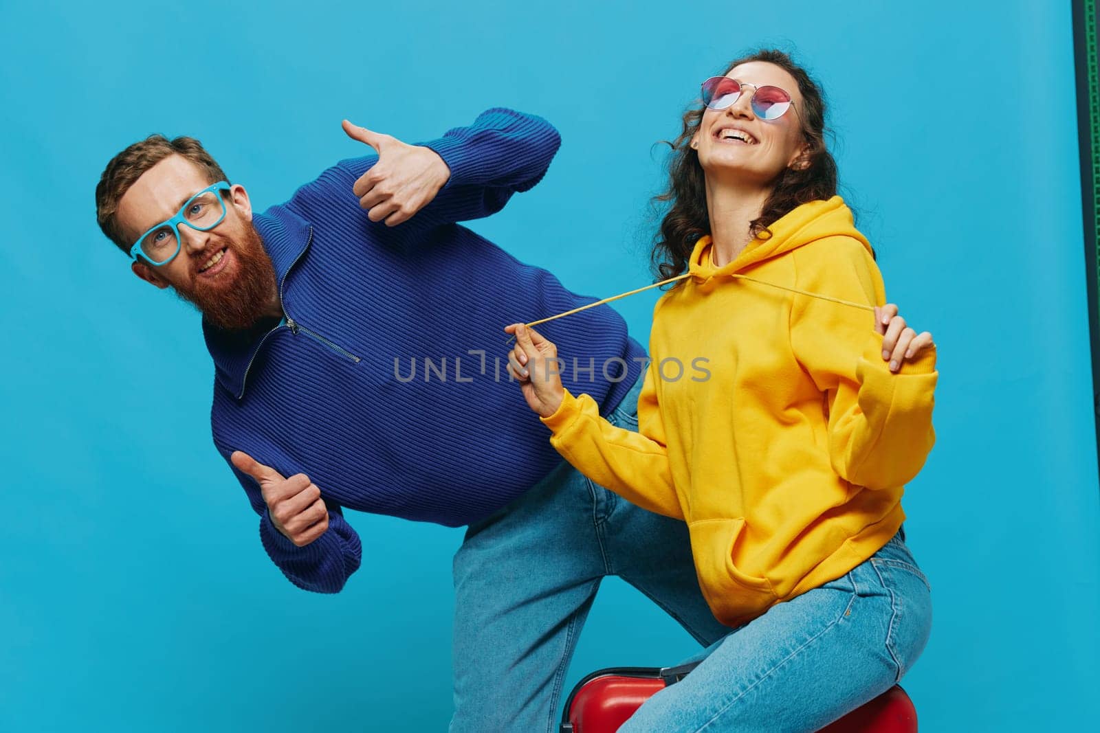 Woman and man smile sitting on suitcase with red suitcase smile, on blue background, packing for trip, family vacation trip. High quality photo