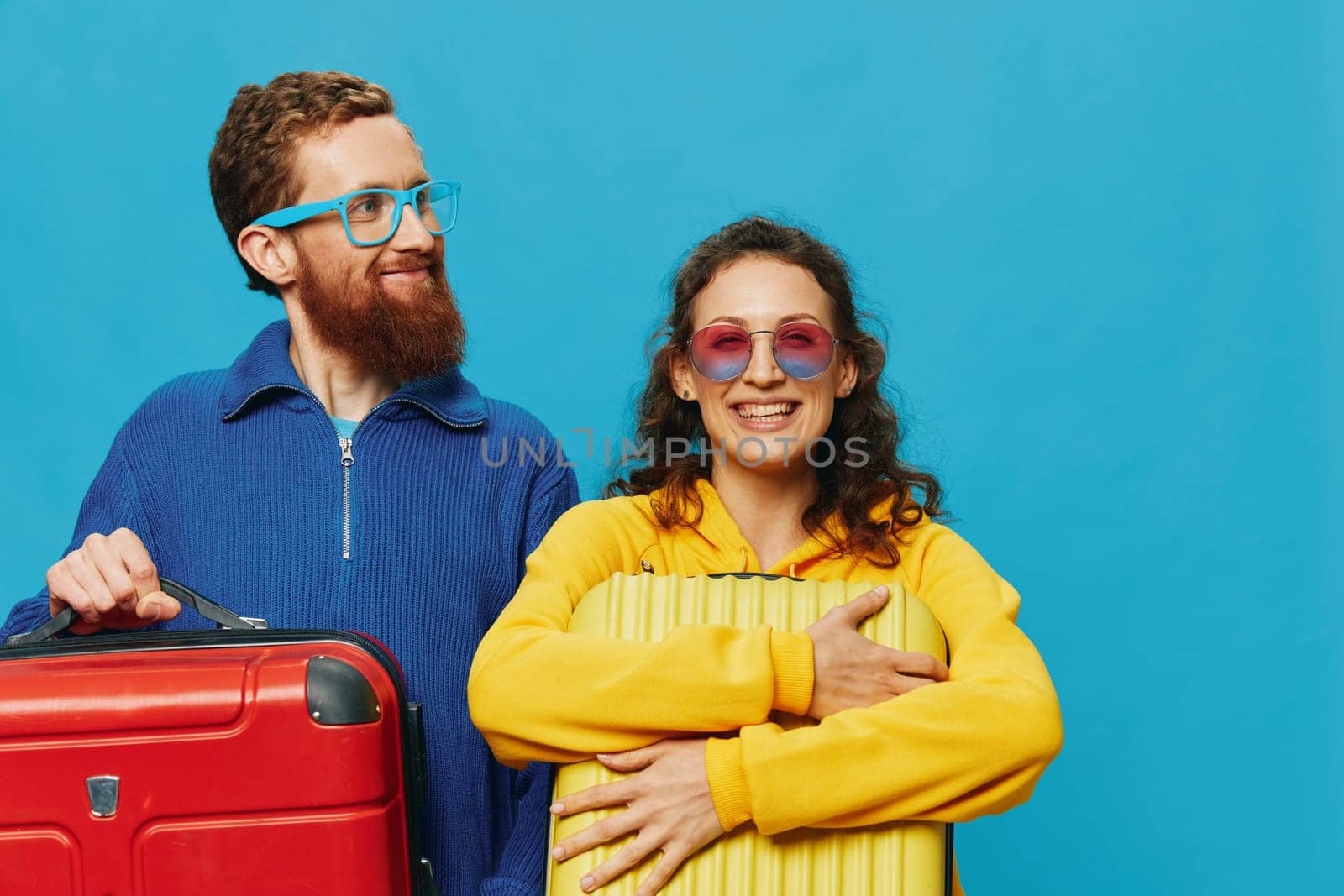 Woman and man smile suitcases in hand with yellow and red suitcase smile fun, on blue background, packing for a trip, family vacation trip. by SHOTPRIME