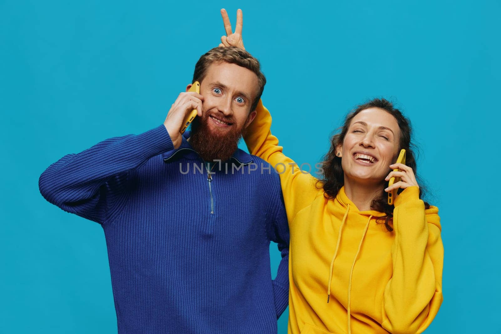 Woman and man cheerful couple with phones in their hands crooked smile cheerful, on blue background. The concept of real family relationships, talking on the phone, work online. by SHOTPRIME