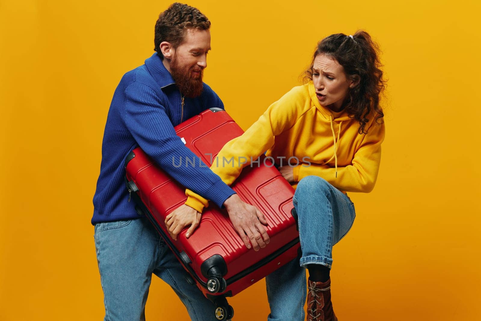 Woman and man smiling, suitcases in hand with yellow and red suitcase smiling merrily and crooked, yellow background, going on a trip, family vacation trip, newlyweds. by SHOTPRIME