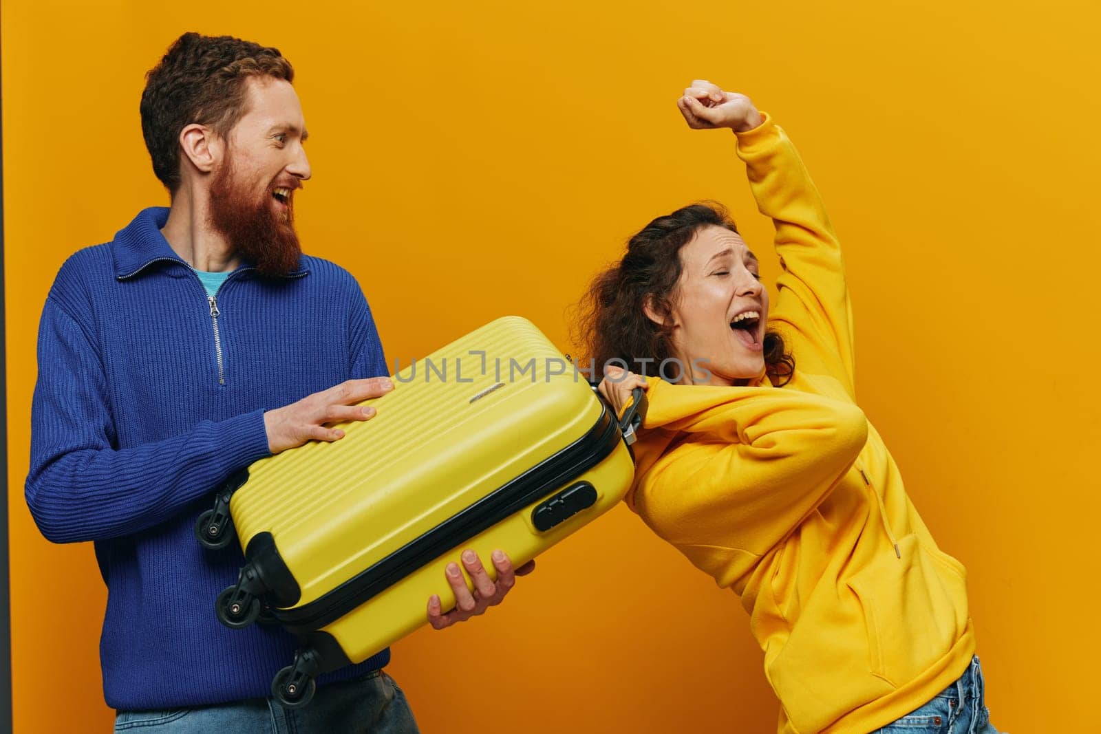 Woman and man smiling, suitcases in hand with yellow and red suitcase smiling merrily and crooked, yellow background, going on a trip, family vacation trip, newlyweds. High quality photo