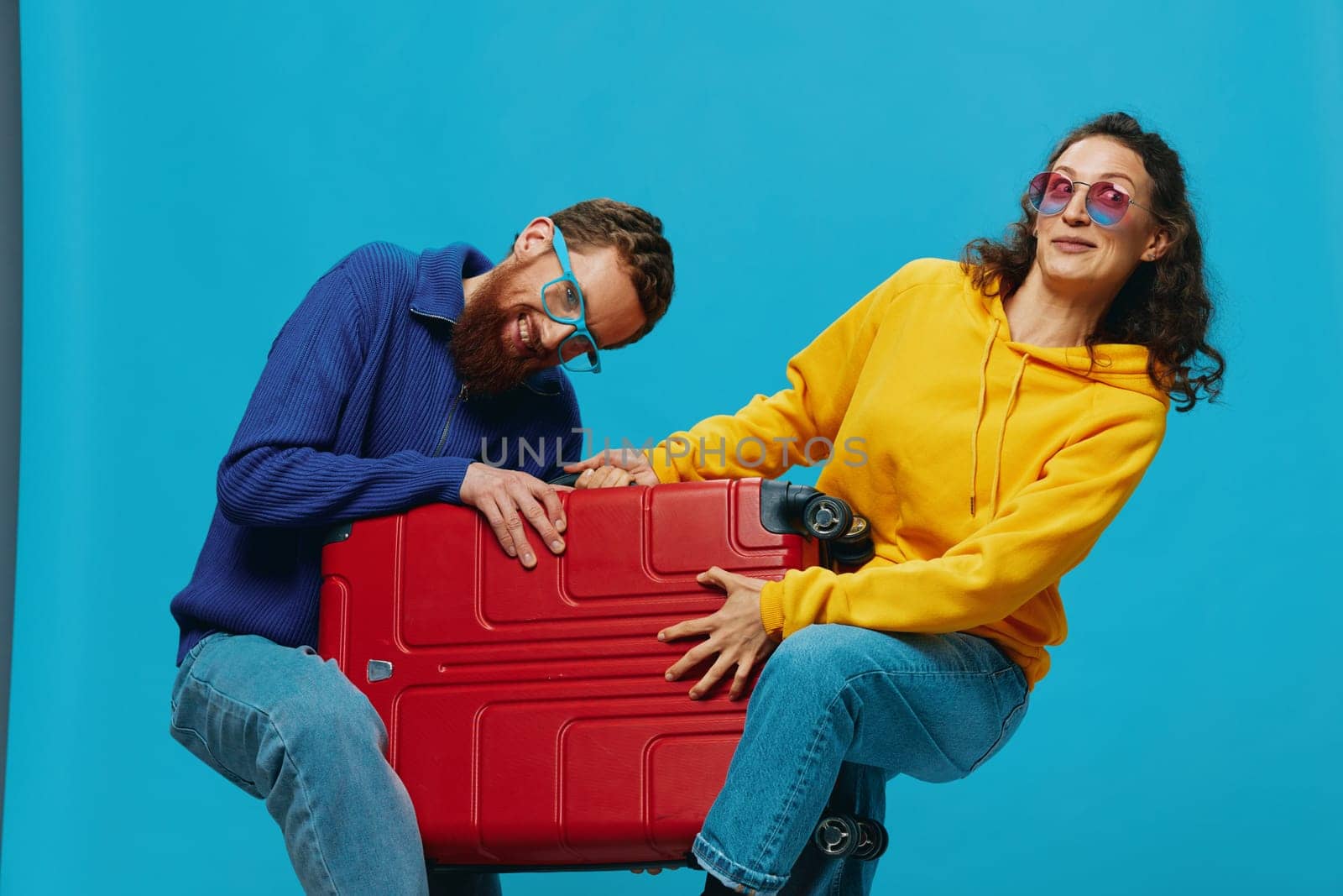 Woman and man smile suitcases in hand with yellow and red suitcase smile fun, on blue background, packing for a trip, family vacation trip. by SHOTPRIME