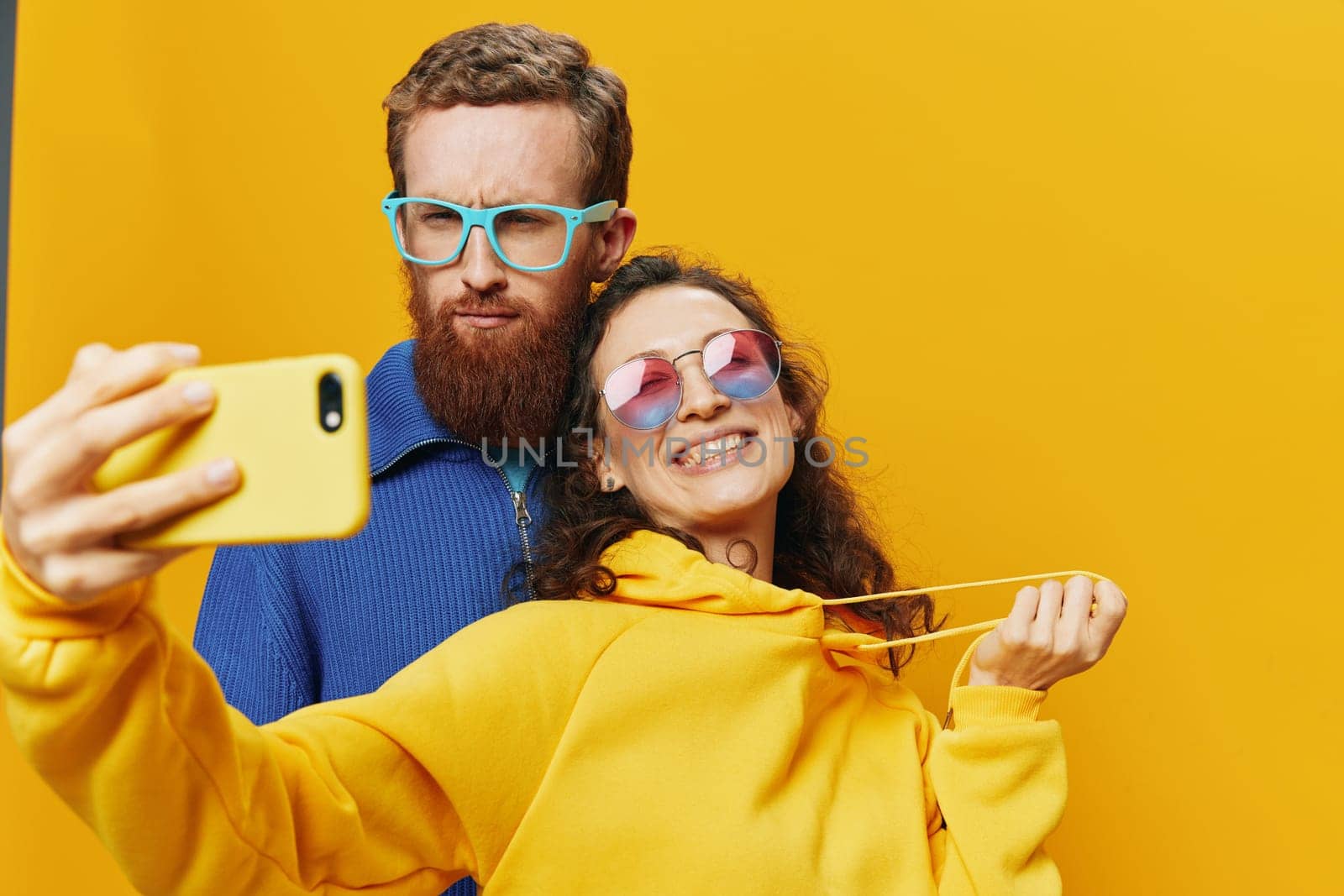 Woman and man funny couple with phones in hand social networking and communication crooked do selfies smile fun, on yellow background. The concept of real family relationships, freelancers, work online. High quality photo