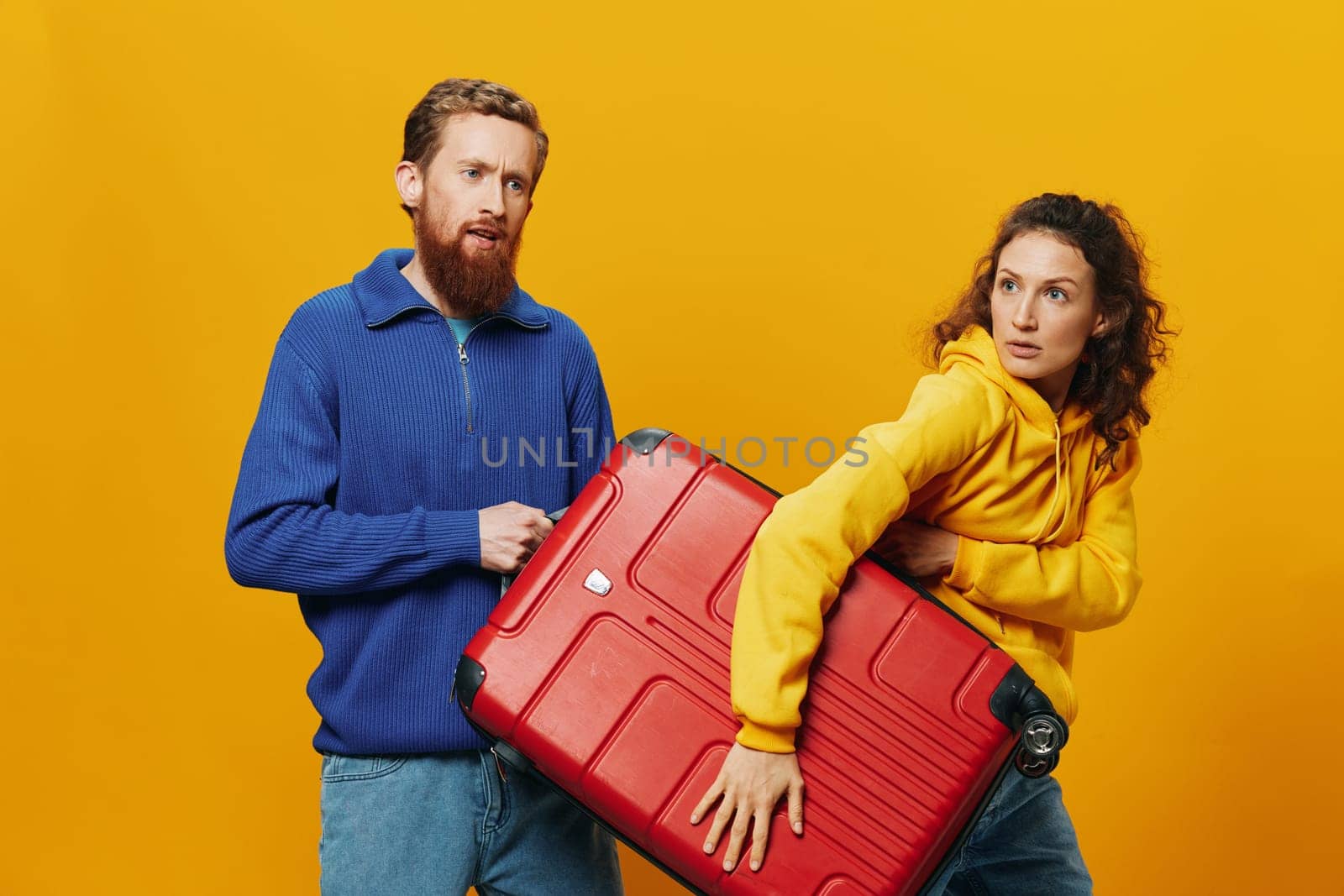 Woman and man smiling, suitcases in hand with yellow and red suitcase smiling merrily and crooked, yellow background, going on a trip, family vacation trip, newlyweds. High quality photo