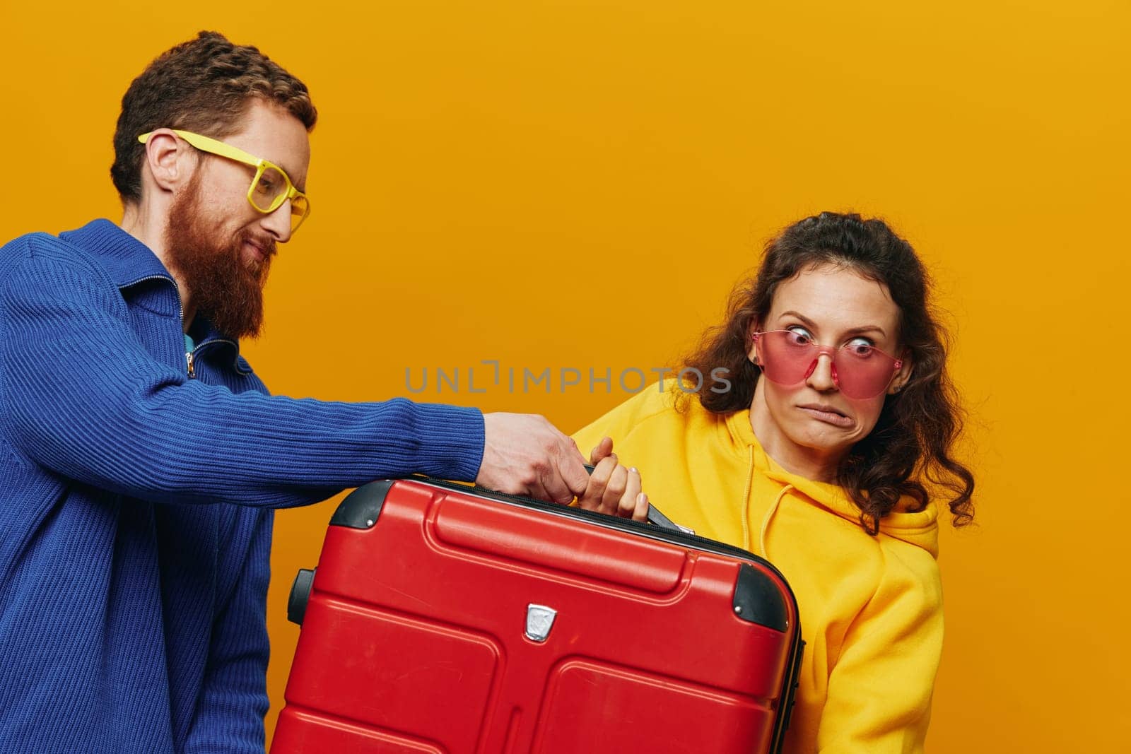 Woman and man smiling, suitcases in hand with yellow and red suitcase smiling merrily and crooked, yellow background, going on a trip, family vacation trip, newlyweds. by SHOTPRIME