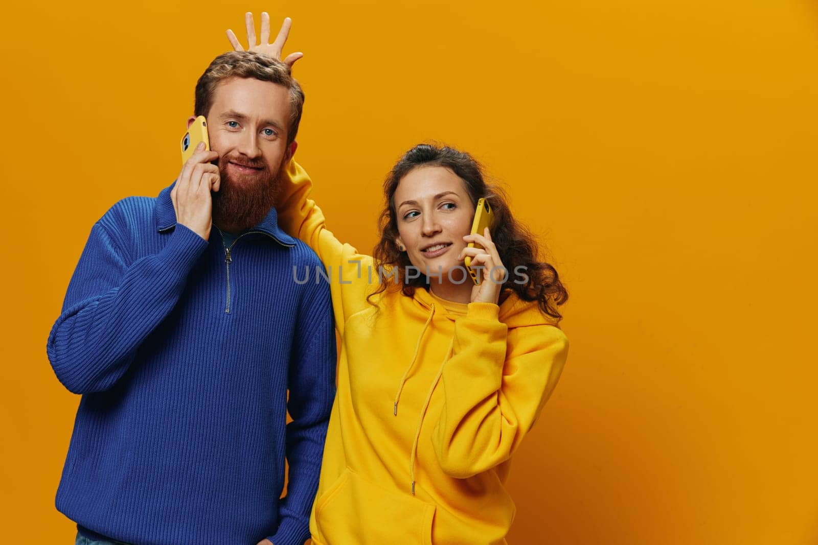 Woman and man cheerful couple with phones in hand talking on cell phone crooked smile cheerful, on yellow background. The concept of real family relationships, talking on the phone, work online. by SHOTPRIME