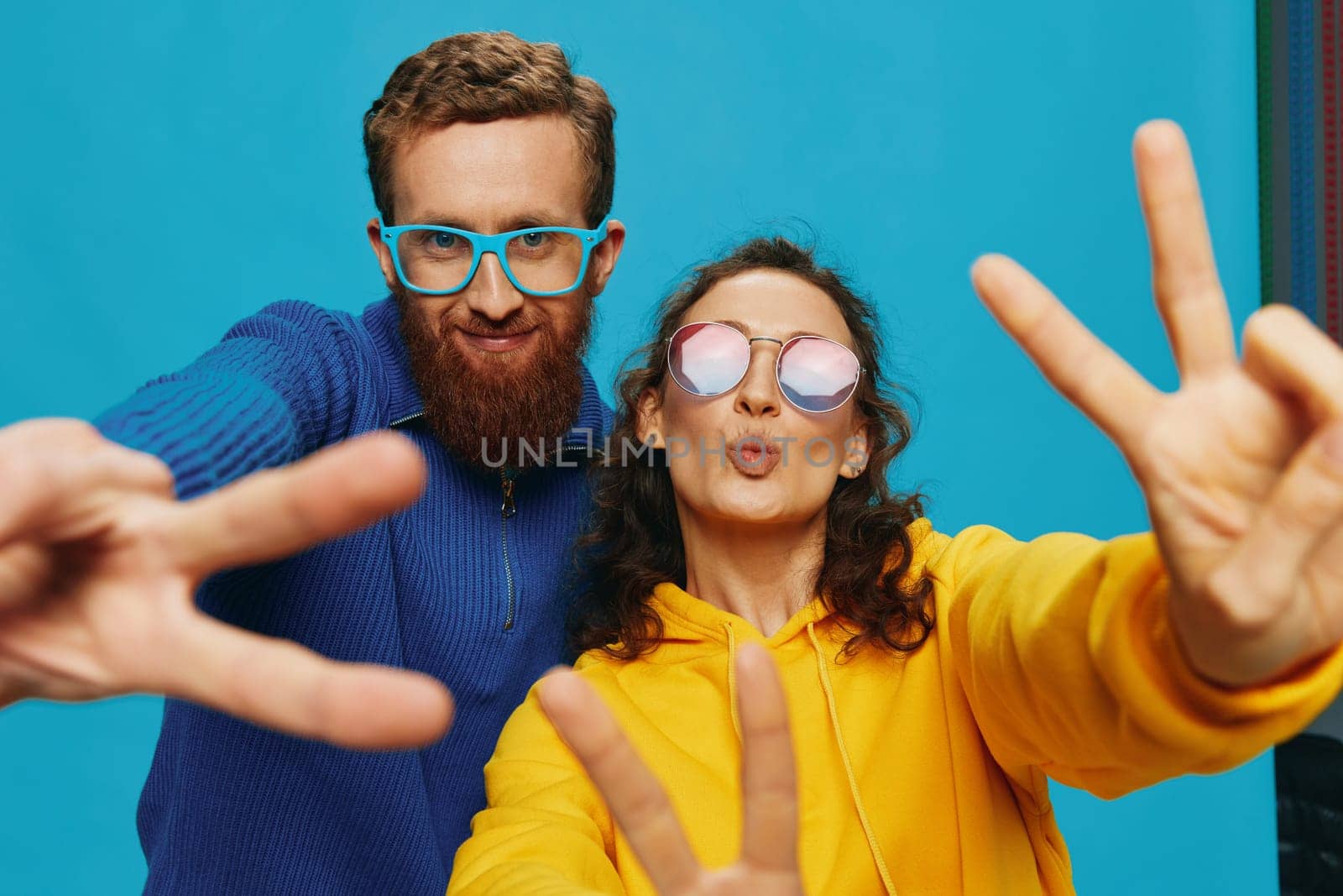 A woman and a man fun couple cranking and showing signs with their hands smiling cheerfully, on a blue background, The concept of a real relationship in a family. by SHOTPRIME