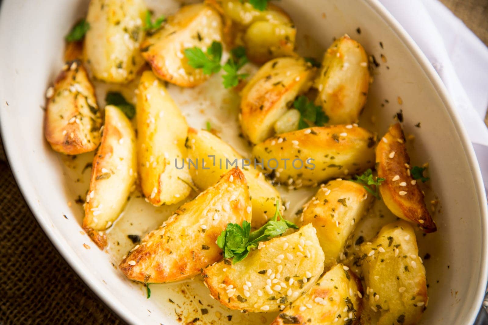 potatoes baked with sesame seeds, herbs and spices in the oven in a ceramic form.