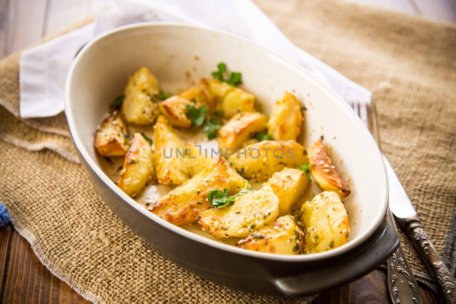 potatoes baked with sesame seeds, herbs and spices in the oven in a ceramic form.
