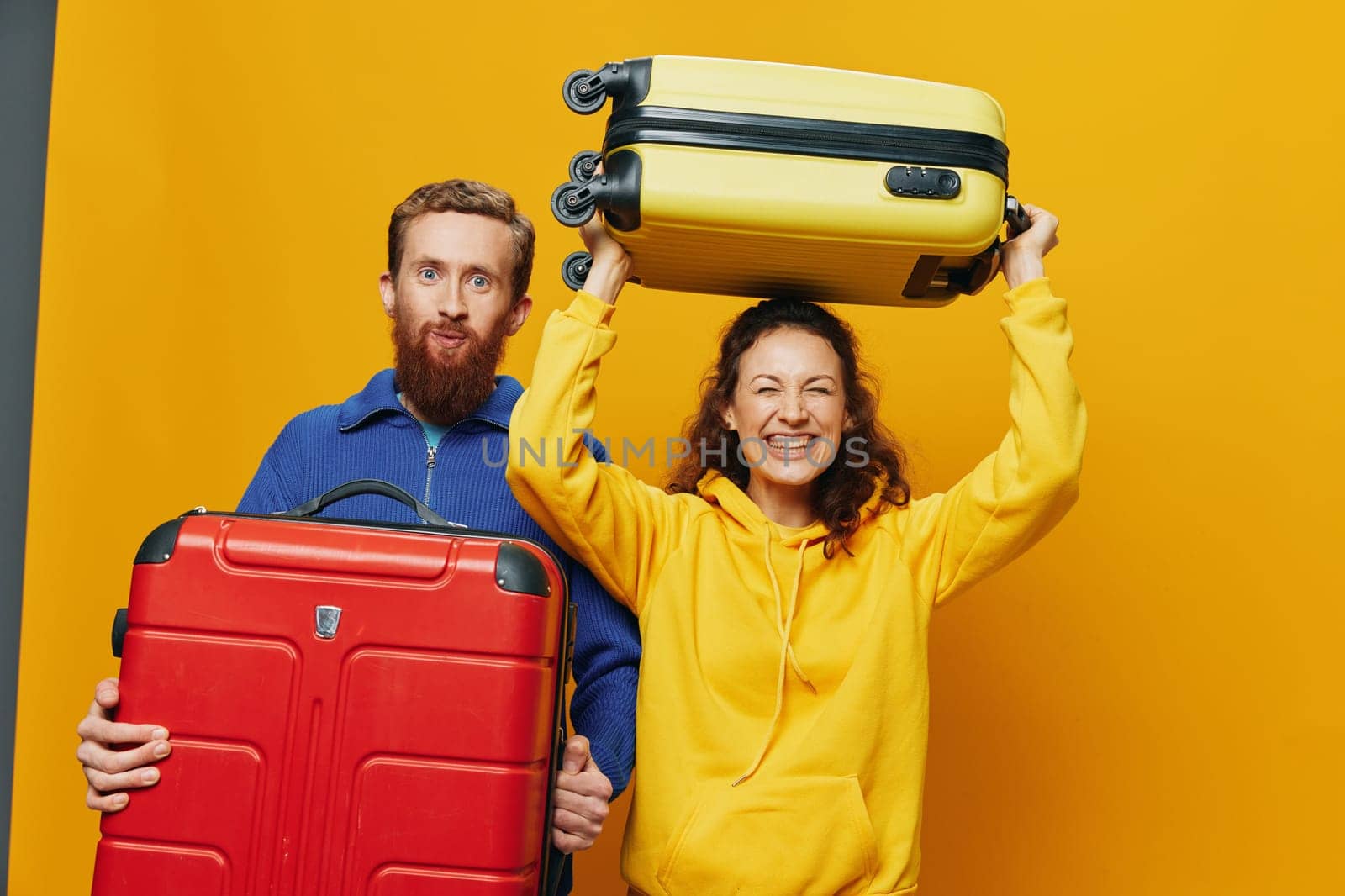 Woman and man smiling, suitcases in hand with yellow and red suitcase smiling merrily and crooked, yellow background, going on a trip, family vacation trip, newlyweds. by SHOTPRIME