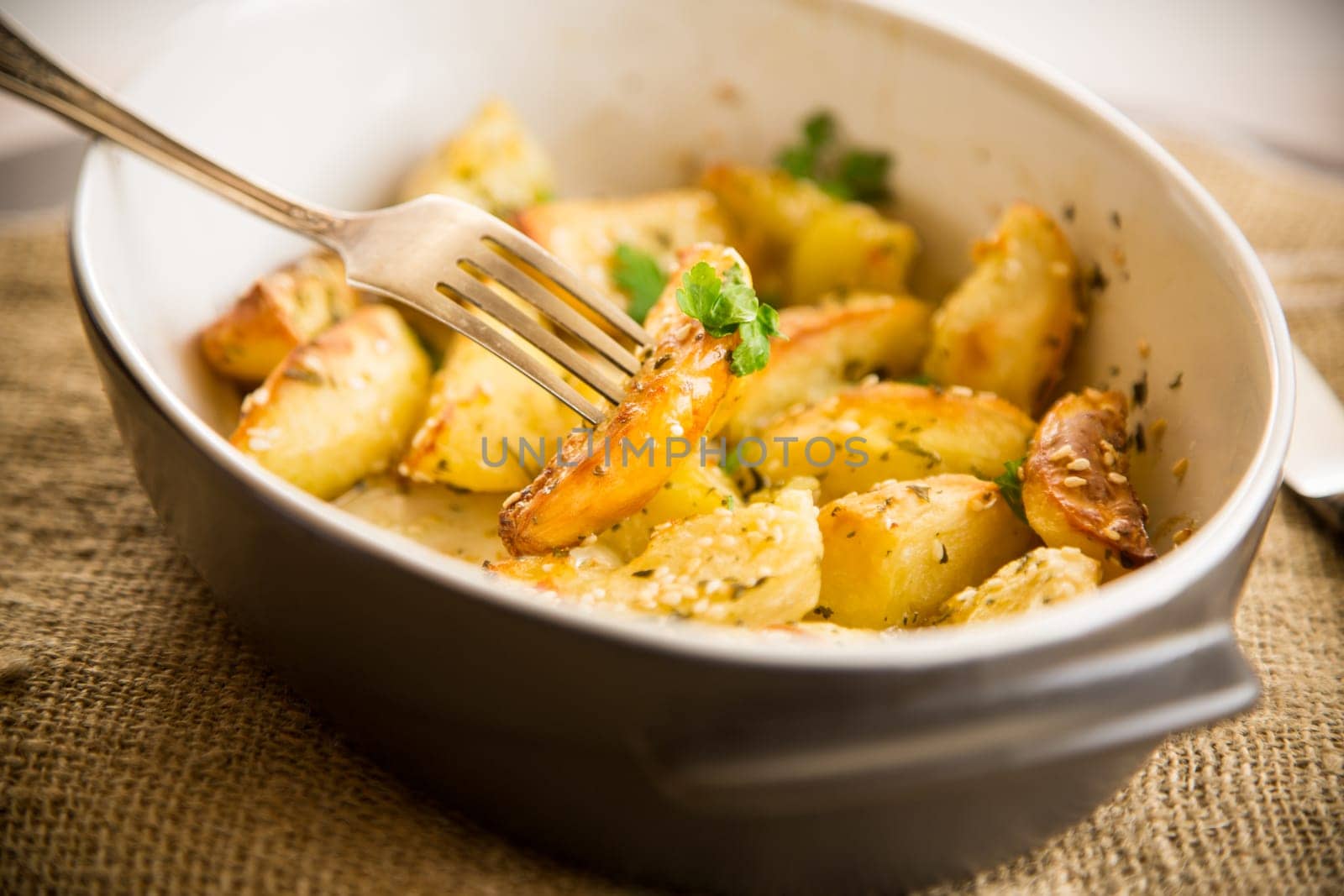 potatoes baked with sesame seeds, herbs and spices in the oven in a ceramic form.