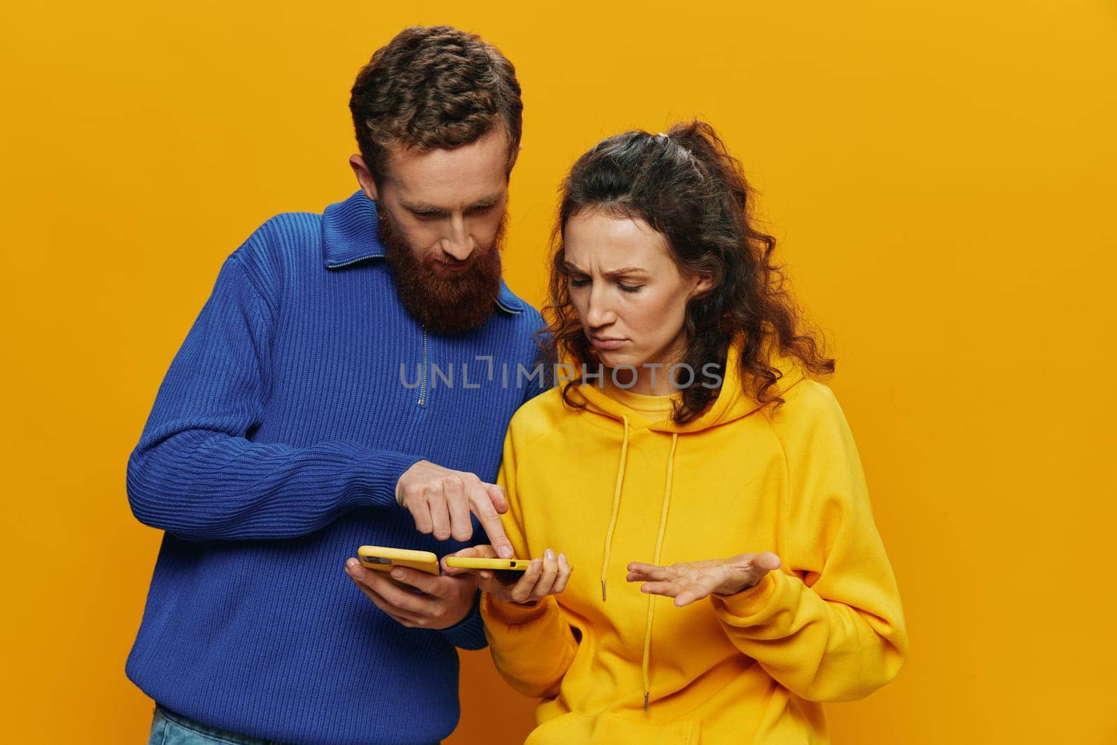 Woman and man cheerful couple with phones in hand social networking and communication crooked smile fun and fight, in yellow background. The concept of real family relationships, freelancers, work online. High quality photo