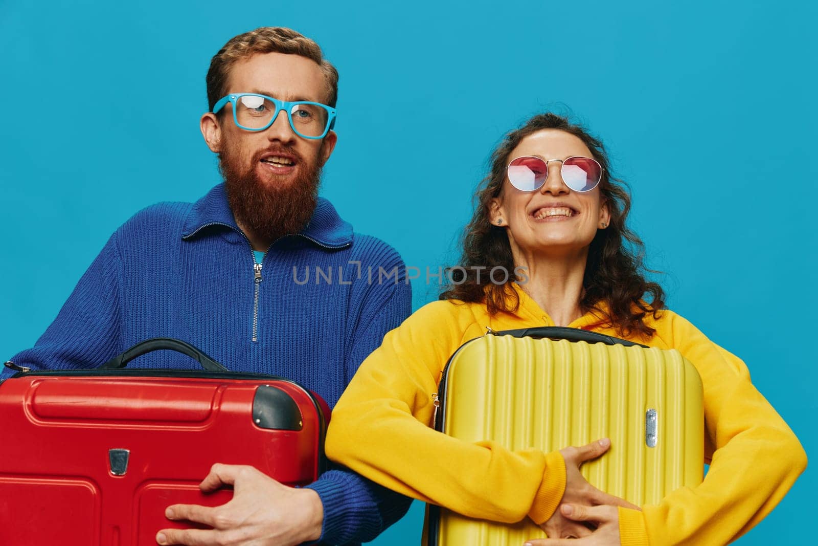 Woman and man smile suitcases in hand with yellow and red suitcase smile fun, on blue background, packing for a trip, family vacation trip. by SHOTPRIME