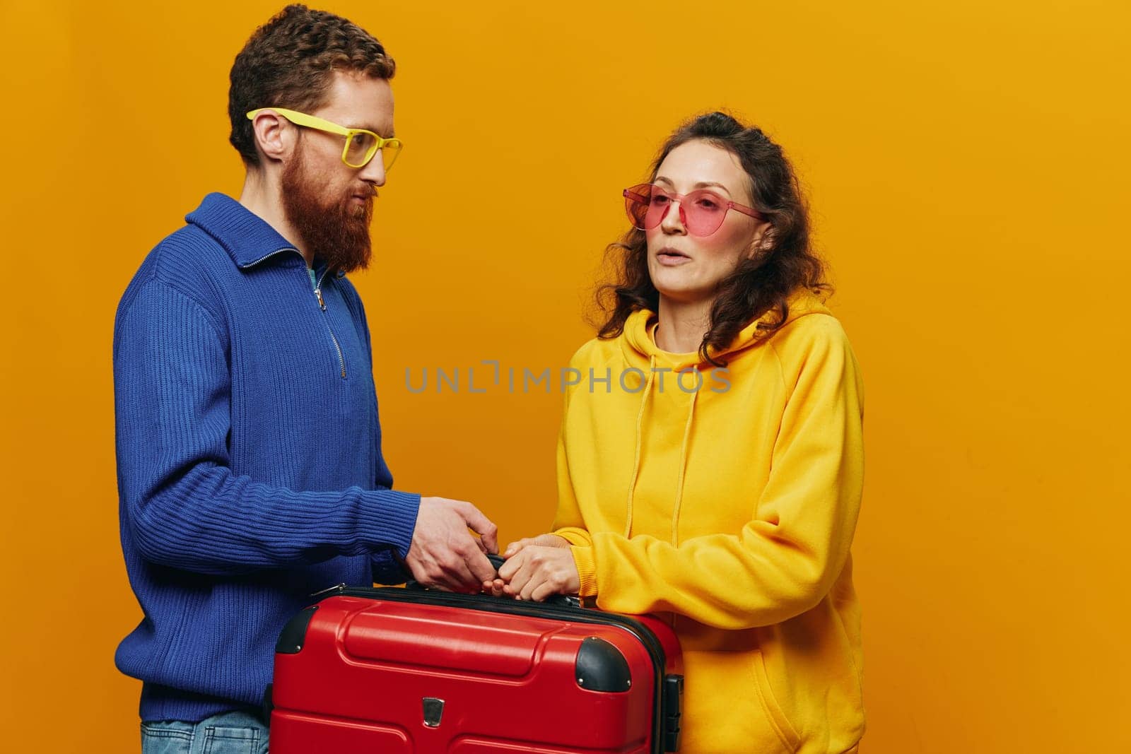 Woman and man smiling, suitcases in hand with yellow and red suitcase smiling merrily and crooked, yellow background, going on a trip, family vacation trip, newlyweds. High quality photo