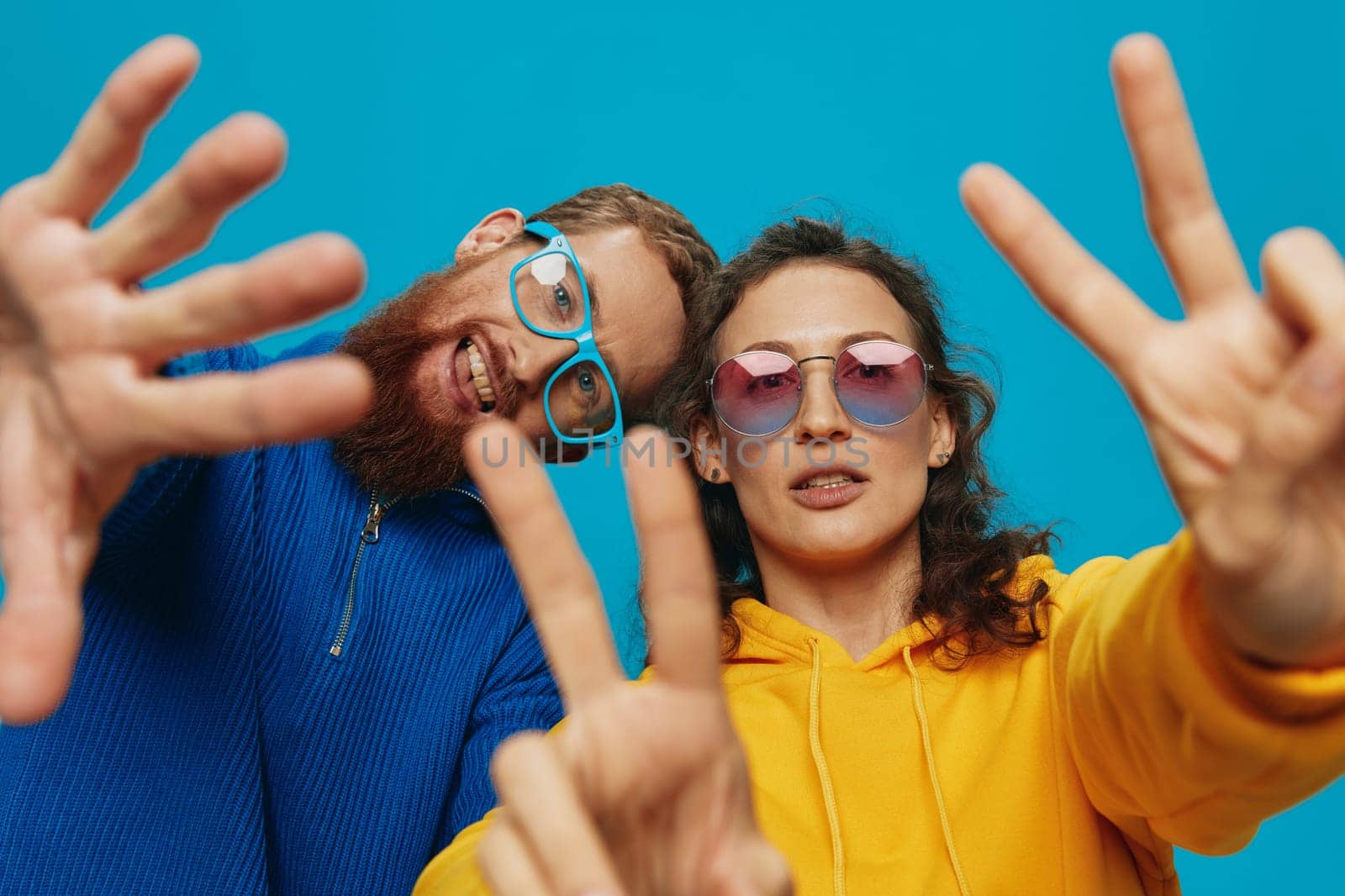 A woman and a man fun couple cranking and showing signs with their hands smiling cheerfully, on a blue background, The concept of a real relationship in a family. by SHOTPRIME