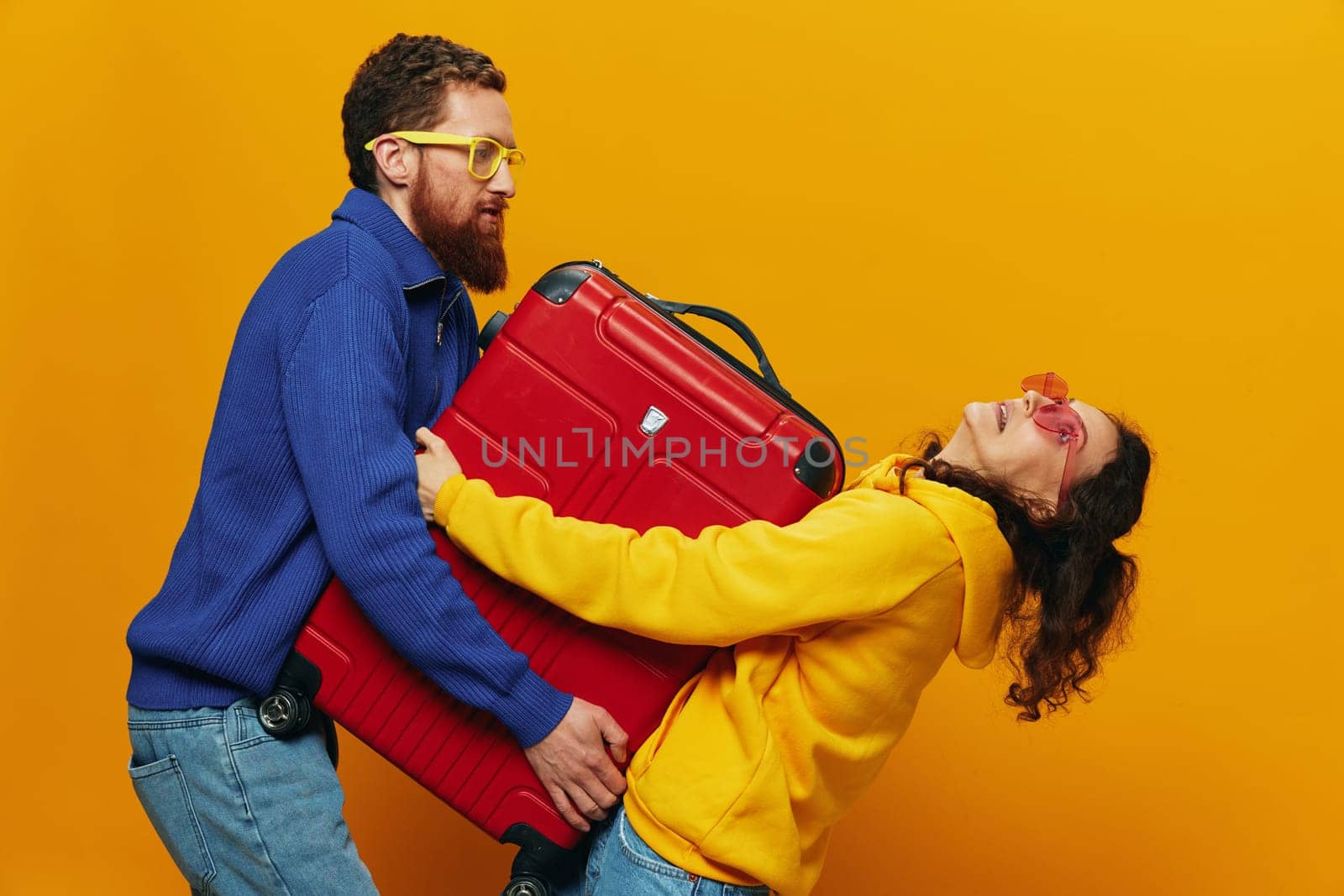 Woman and man smiling, suitcases in hand with yellow and red suitcase smiling merrily and crooked, yellow background, going on a trip, family vacation trip, newlyweds. by SHOTPRIME