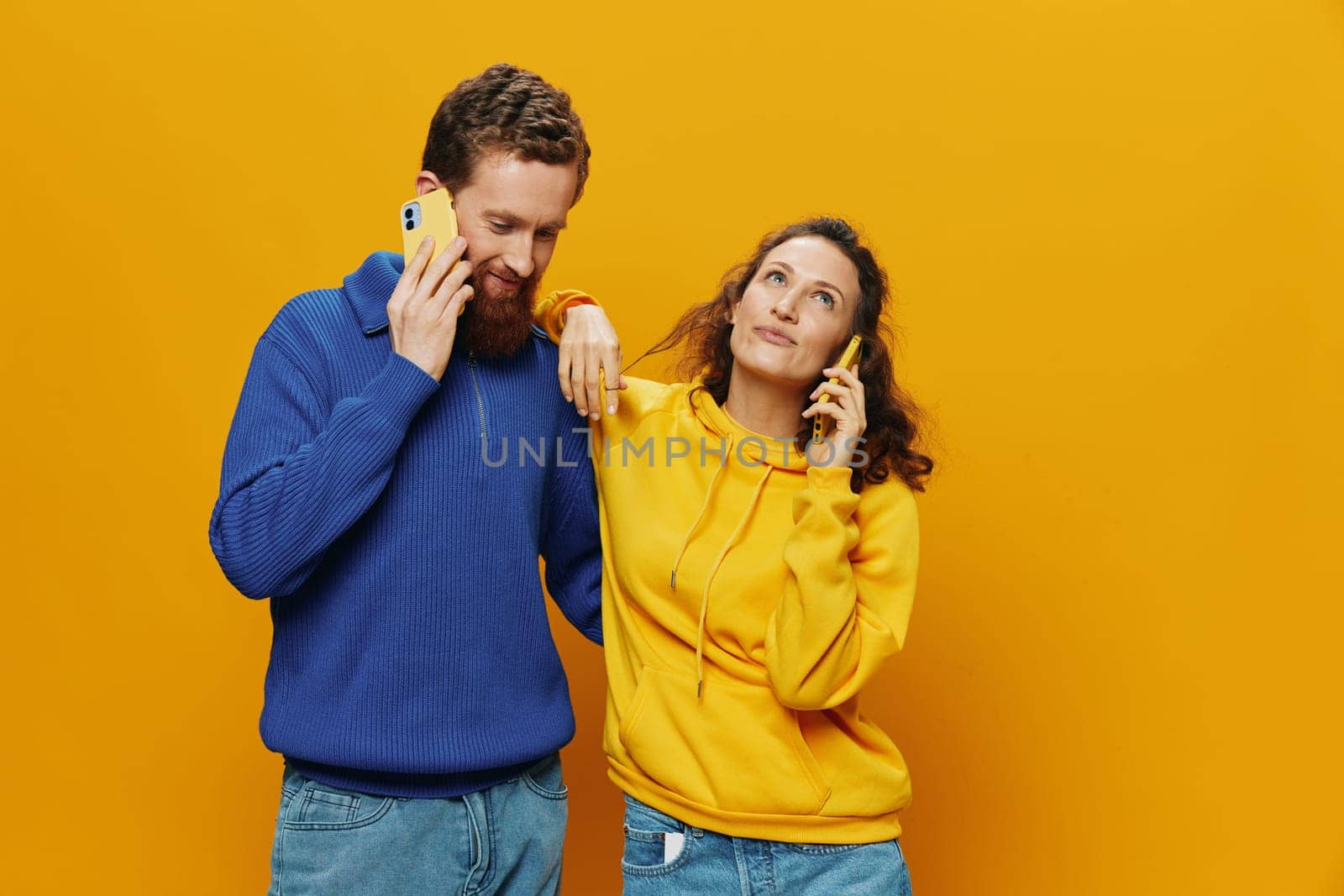 Woman and man cheerful couple with phones in hand talking on cell phone crooked smile cheerful, on yellow background. The concept of real family relationships, talking on the phone, work online. High quality photo