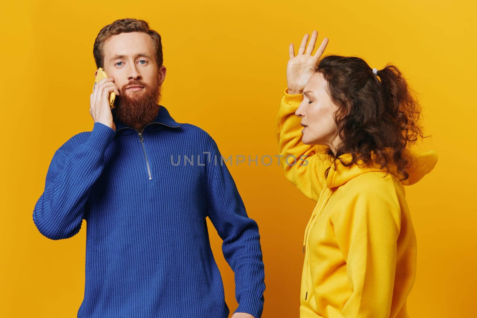 Man and woman couple with phone in hand call talking on the phone, on a yellow background, symbols signs and hand gestures, family quarrel jealousy and scandal. by SHOTPRIME