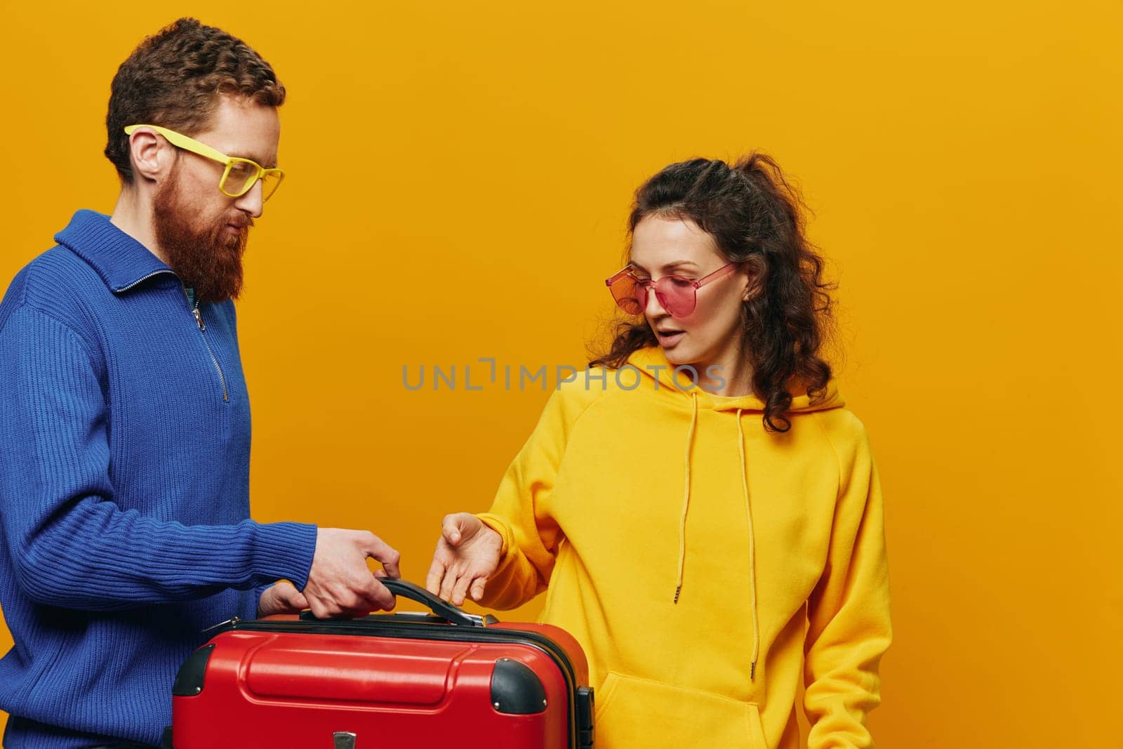 Woman and man smiling, suitcases in hand with yellow and red suitcase smiling merrily and crooked, yellow background, going on a trip, family vacation trip, newlyweds. by SHOTPRIME