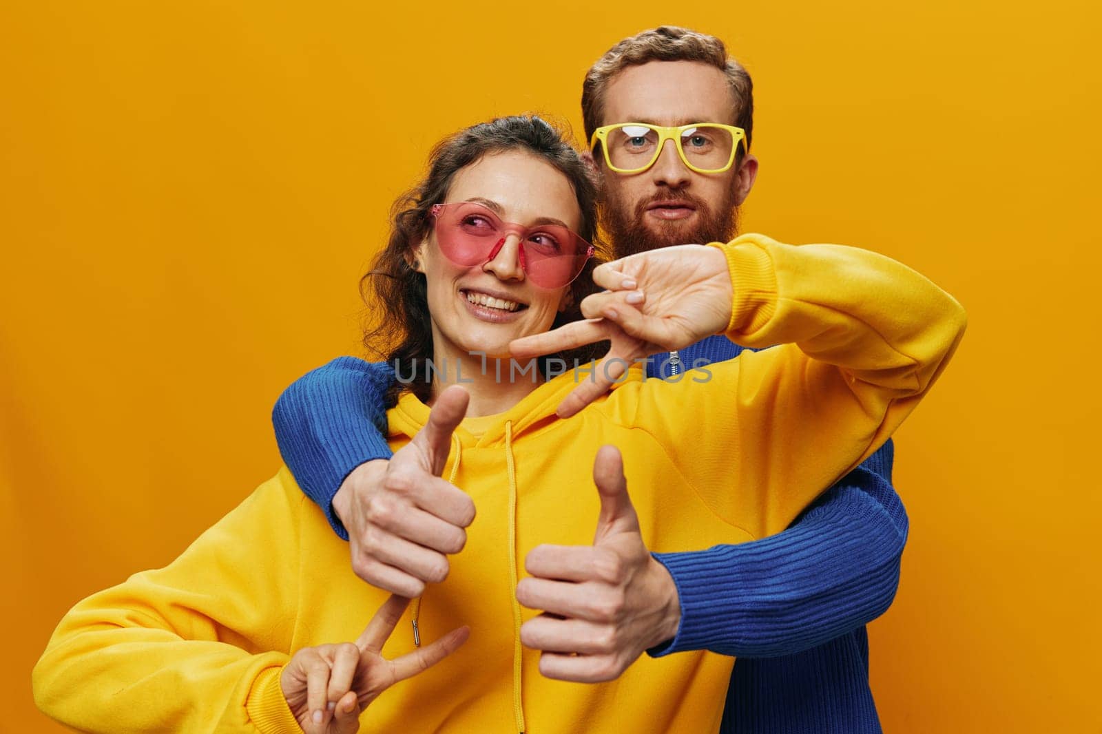 Man and woman couple smiling cheerfully and crooked with glasses, on yellow background, symbols signs and hand gestures, family shoot, newlyweds. High quality photo