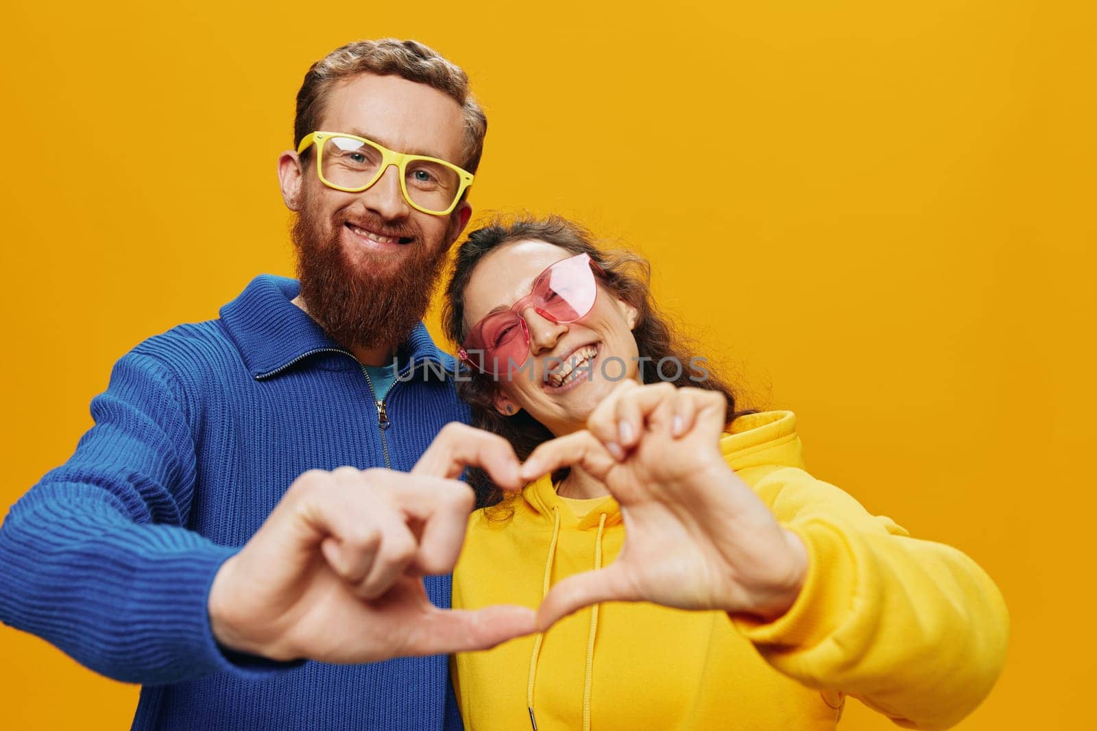 Man and woman couple smiling cheerfully and crooked with glasses, on yellow background, symbols signs and hand gestures, family shoot, newlyweds. High quality photo