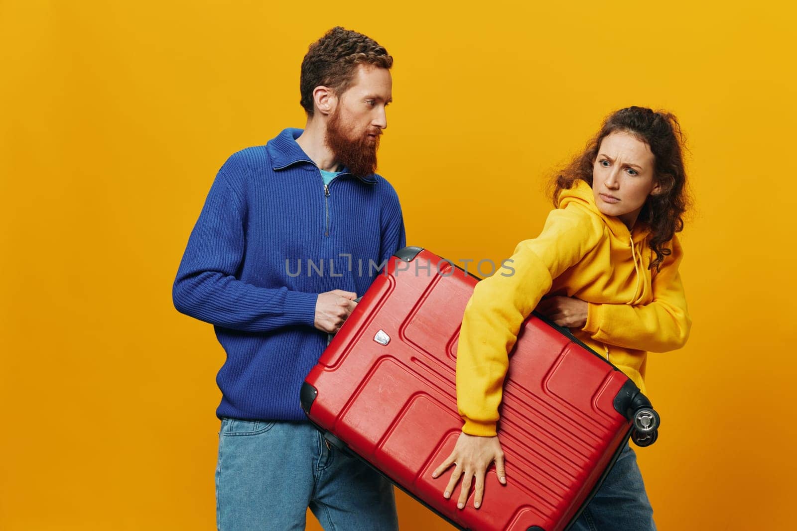 Woman and man smiling, suitcases in hand with yellow and red suitcase smiling merrily and crooked, yellow background, going on a trip, family vacation trip, newlyweds. by SHOTPRIME