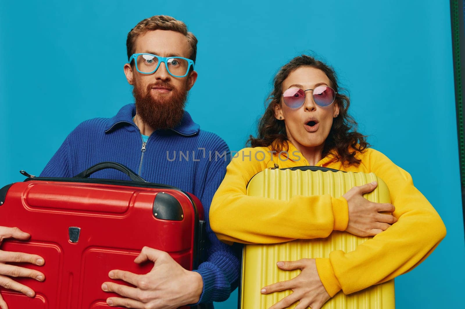 Woman and man smile suitcases in hand with yellow and red suitcase smile fun, on blue background, packing for a trip, family vacation trip. by SHOTPRIME