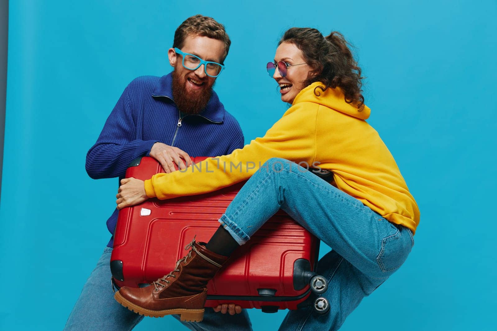 Woman and man smile suitcases in hand with yellow and red suitcase smile fun, on blue background, packing for a trip, family vacation trip. High quality photo