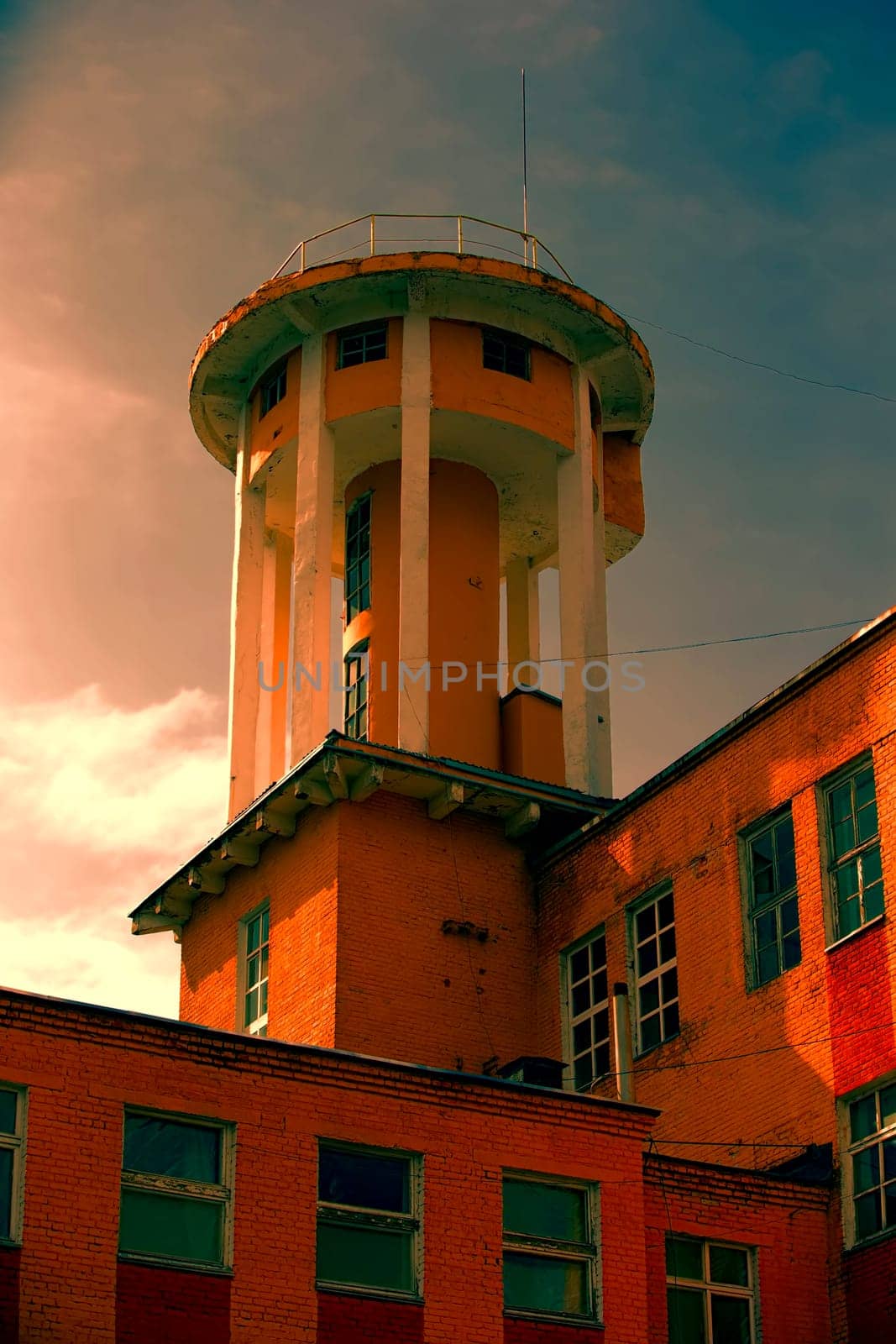 Creative old building with a tower against the background of the evening sky.Old factory