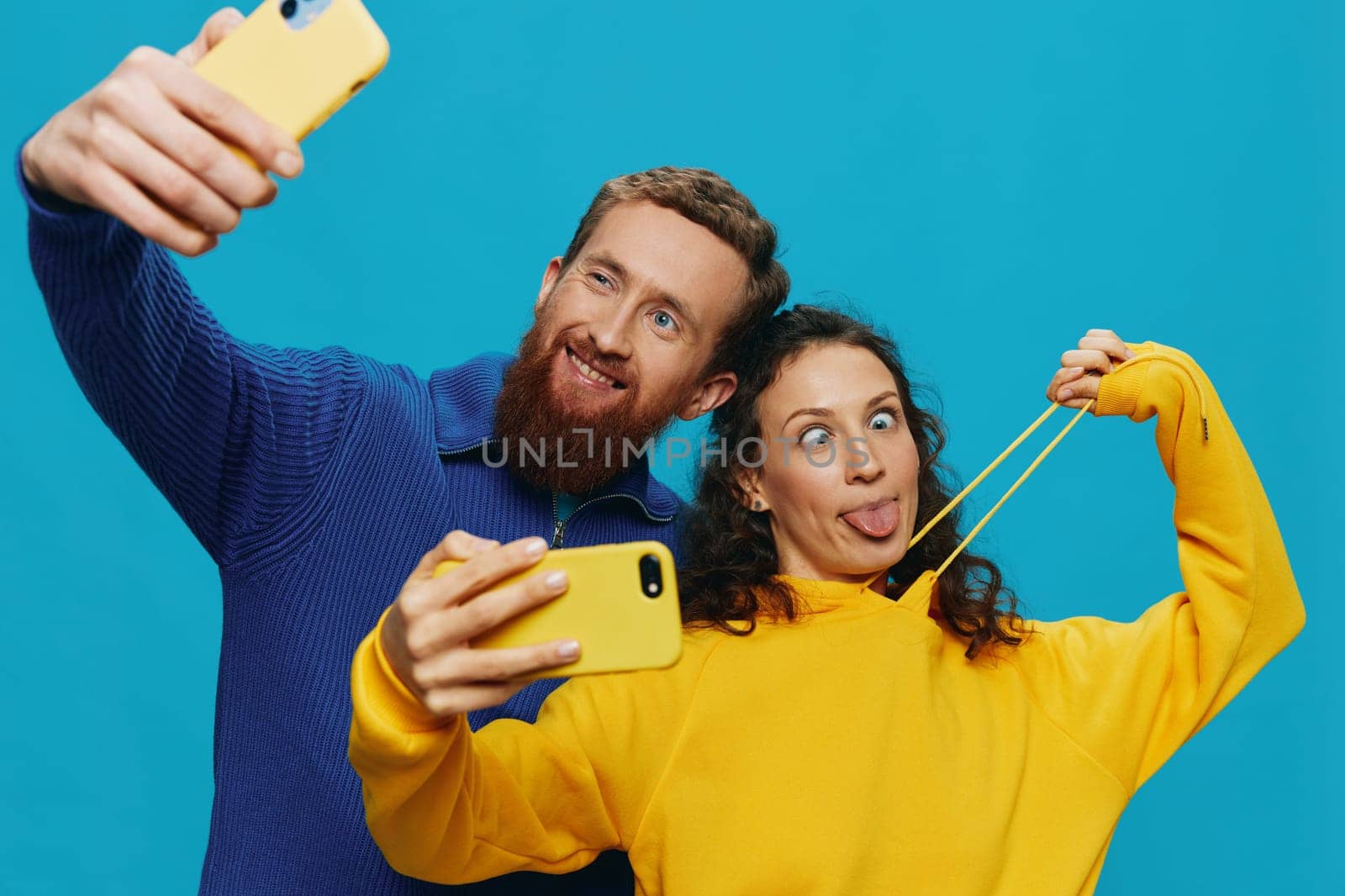 Woman and man funny couple with phones in hand taking selfies crooked smile fun, on blue background. The concept of real family relationships, talking on the phone, work online. by SHOTPRIME