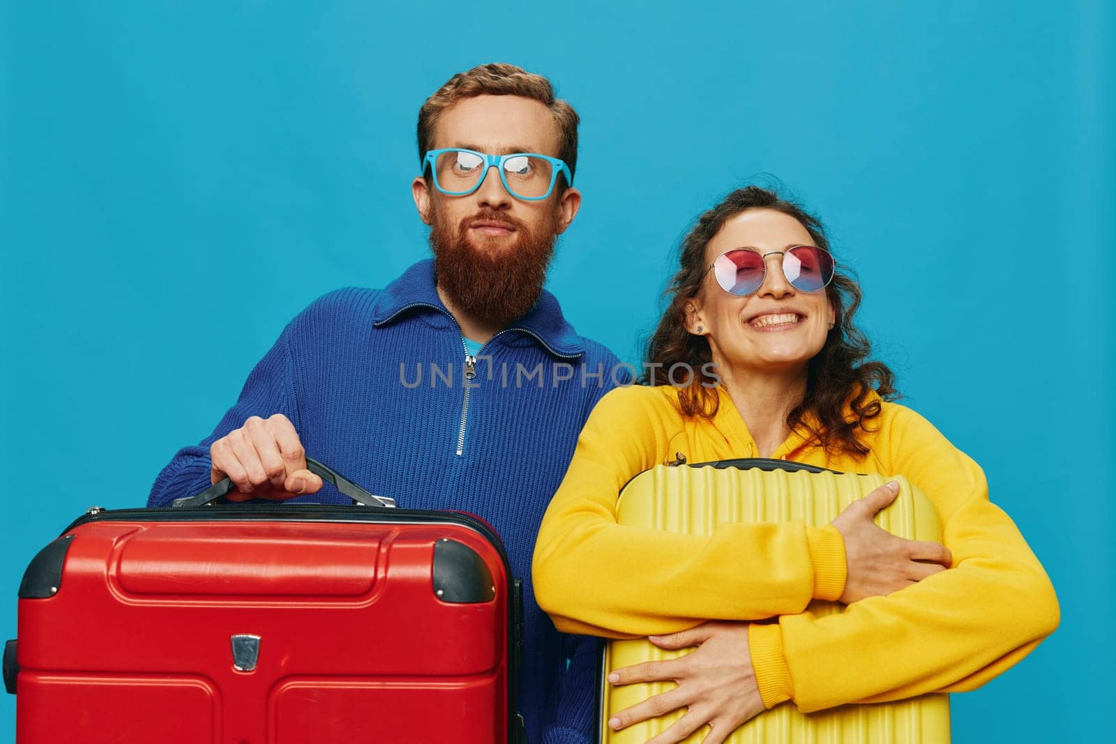 Woman and man smile suitcases in hand with yellow and red suitcase smile fun, on blue background, packing for a trip, family vacation trip. High quality photo