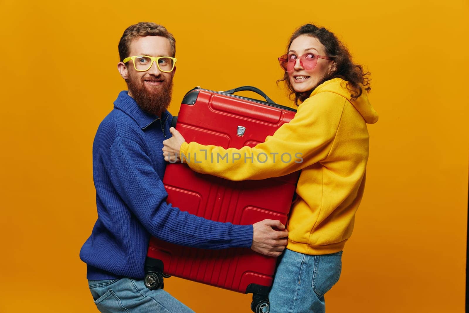 Woman and man smiling, suitcases in hand with yellow and red suitcase smiling merrily and crooked, yellow background, going on a trip, family vacation trip, newlyweds. High quality photo