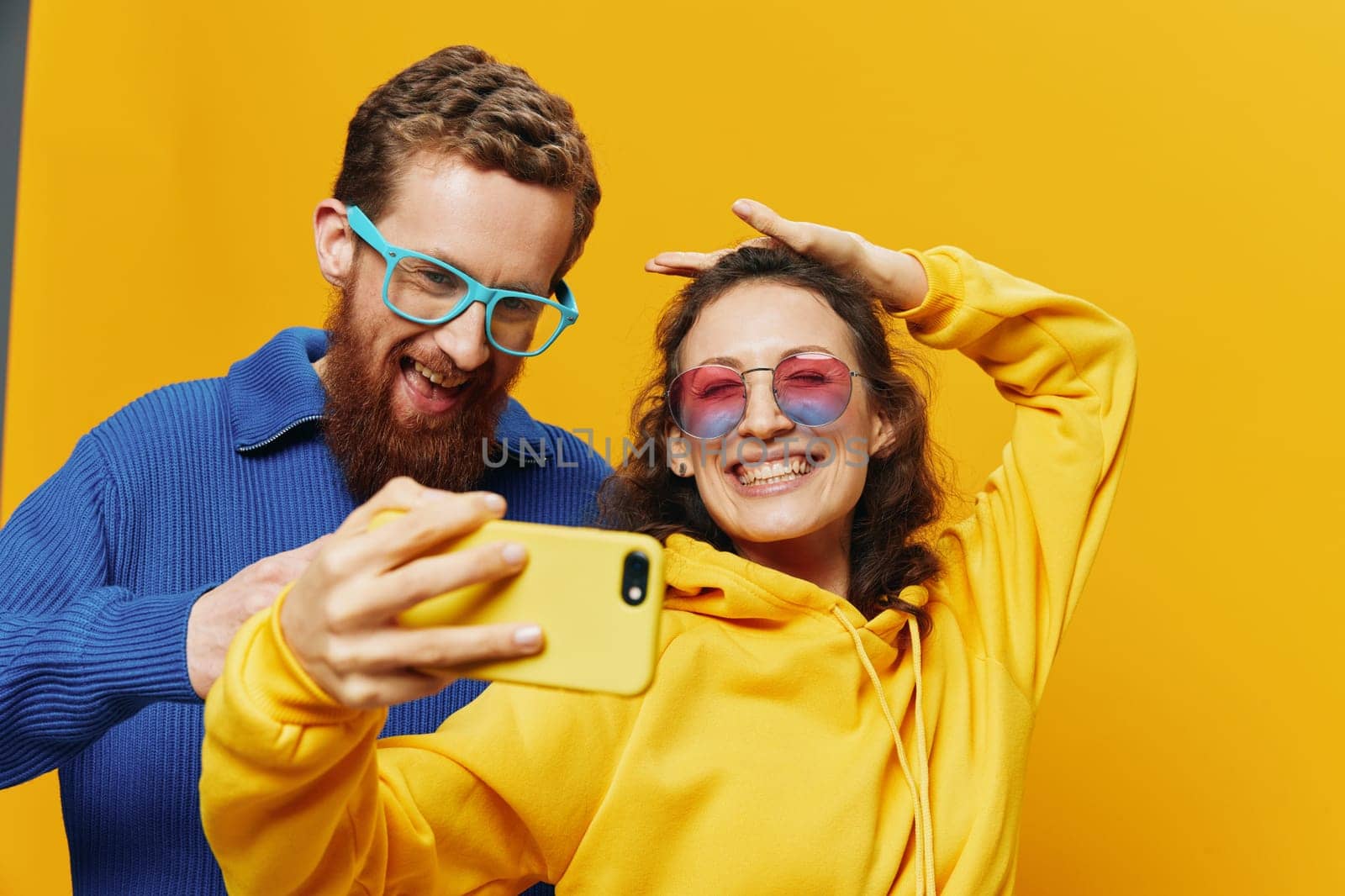 Woman and man funny couple with phones in hand social networking and communication crooked do selfies smile fun, on yellow background. The concept of real family relationships, freelancers, work online. High quality photo
