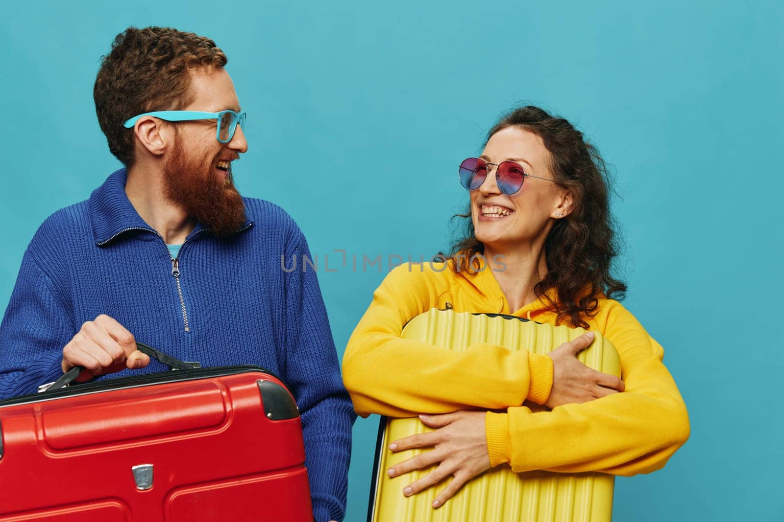 Woman and man smile suitcases in hand with yellow and red suitcase smile fun, on blue background, packing for a trip, family vacation trip. by SHOTPRIME