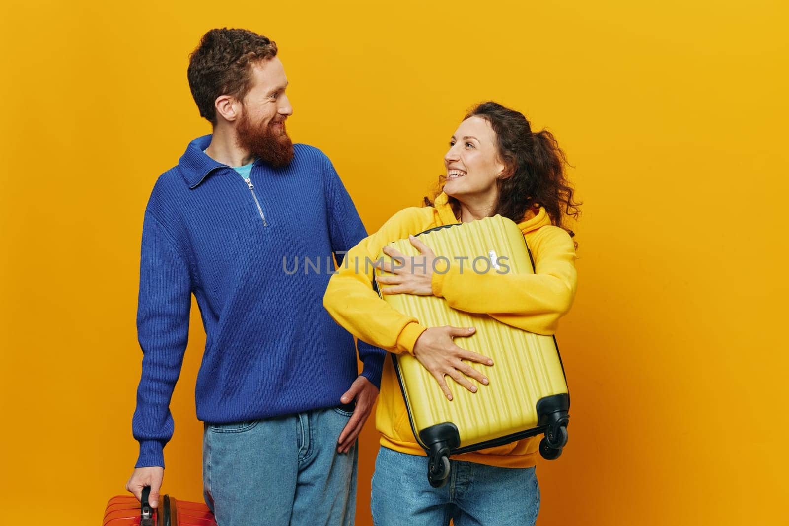 Woman and man smiling, suitcases in hand with yellow and red suitcase smiling merrily and crooked, yellow background, going on a trip, family vacation trip, newlyweds. by SHOTPRIME