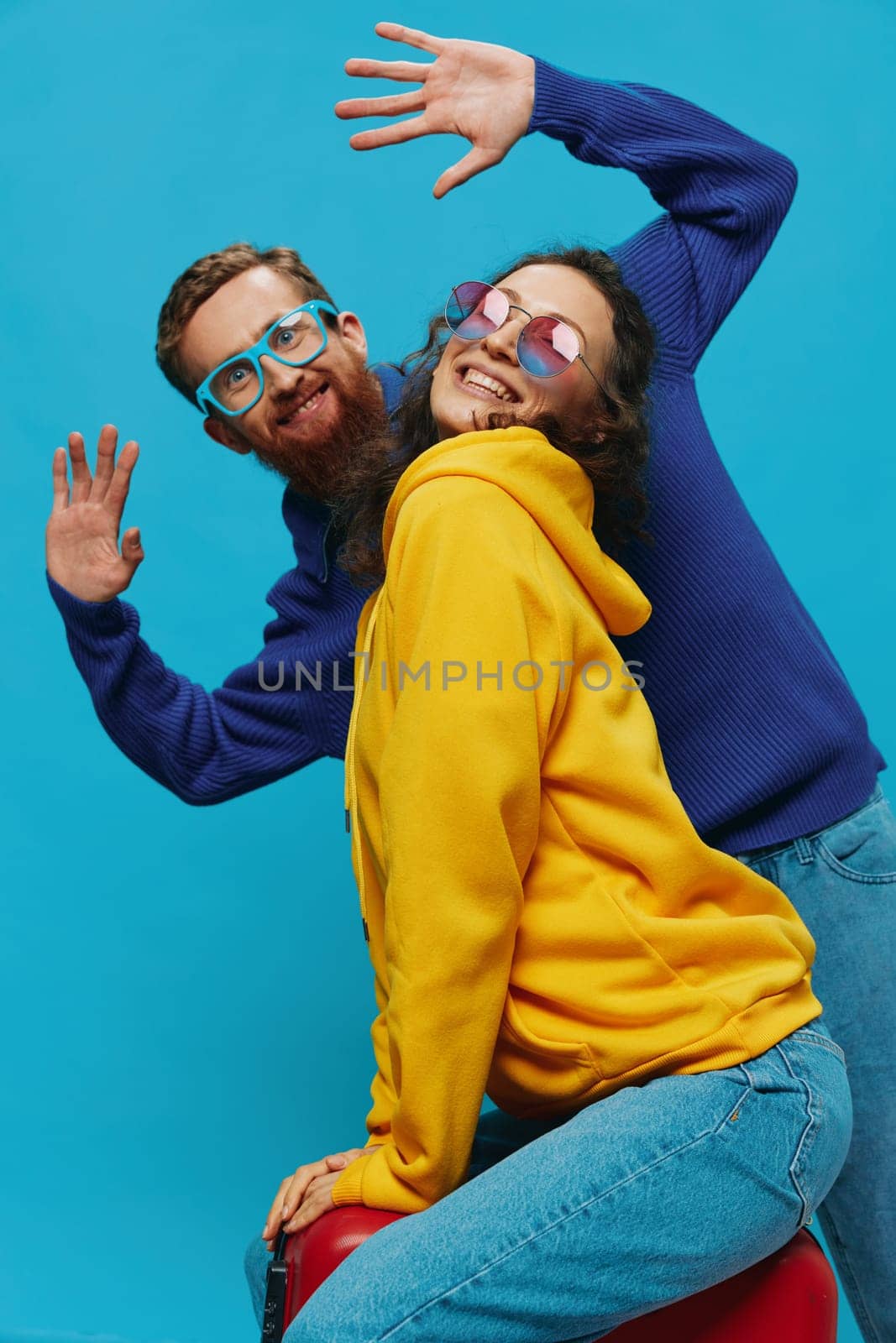 Woman and man smile sitting on suitcase with red suitcase smile, on blue background, packing for trip, family vacation trip. by SHOTPRIME