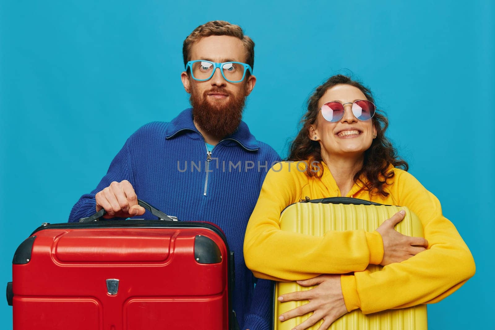 Woman and man smile suitcases in hand with yellow and red suitcase smile fun, on blue background, packing for a trip, family vacation trip. High quality photo