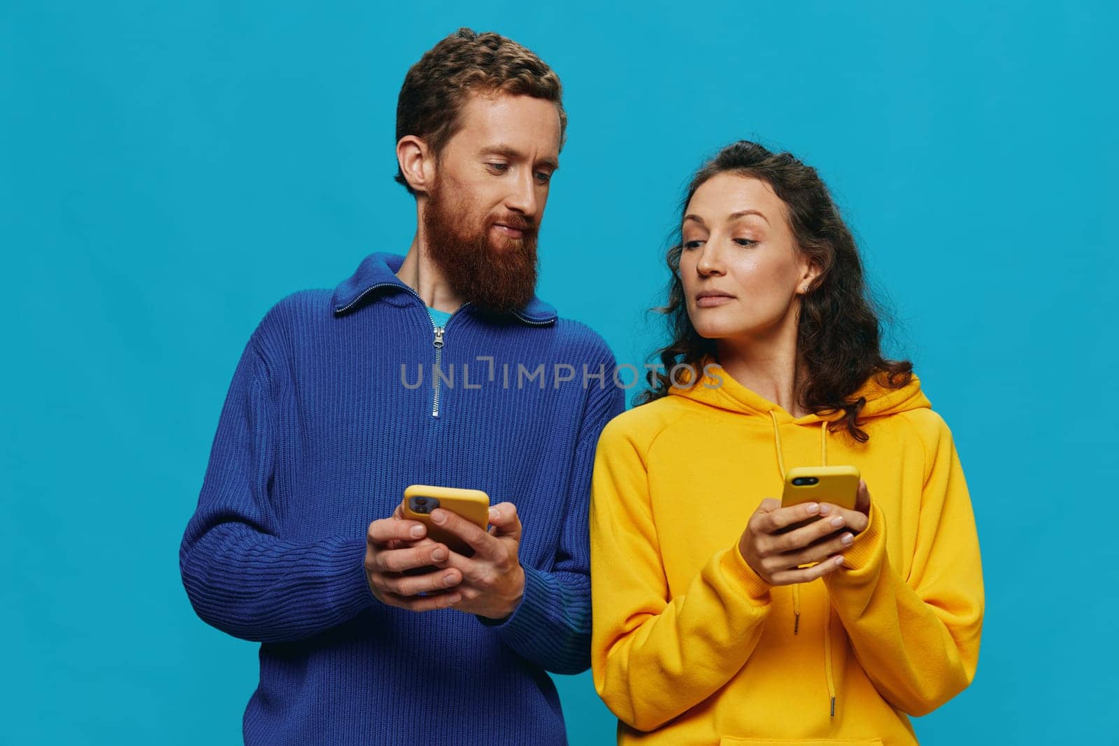 Woman and man cheerful couple with phones in their hands crooked smile cheerful, on blue background. The concept of real family relationships, talking on the phone, work online. High quality photo