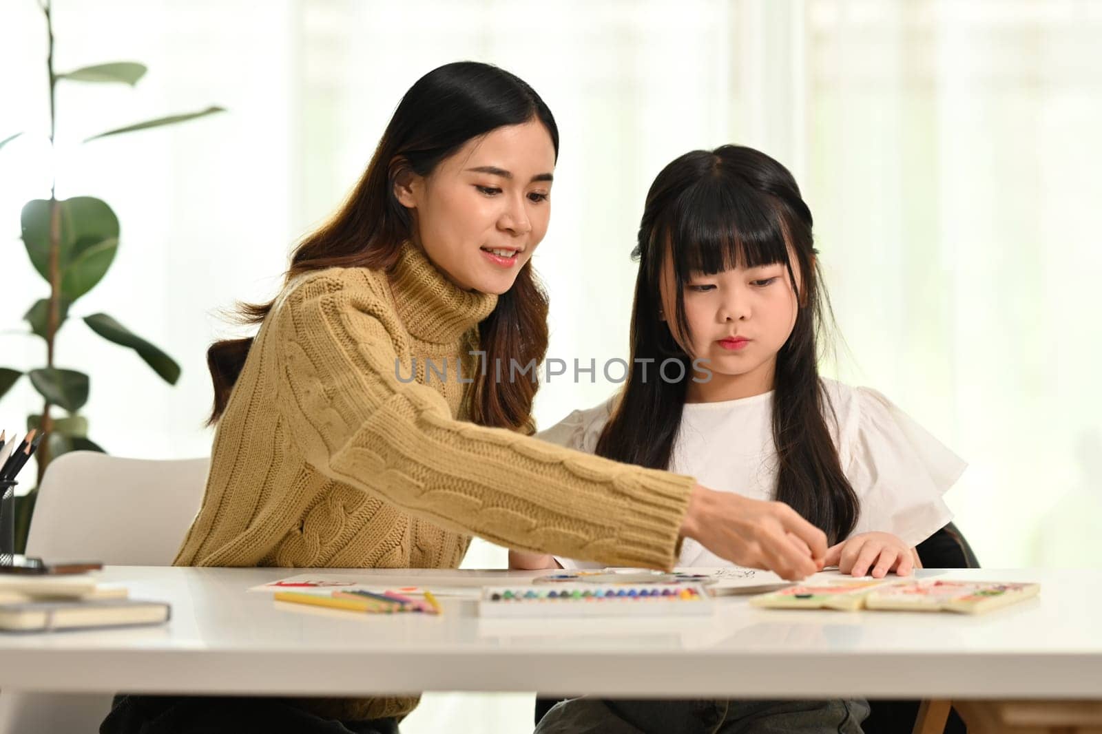 Loving asian mom drawing with her little daughter living room. Family home leisure concept.