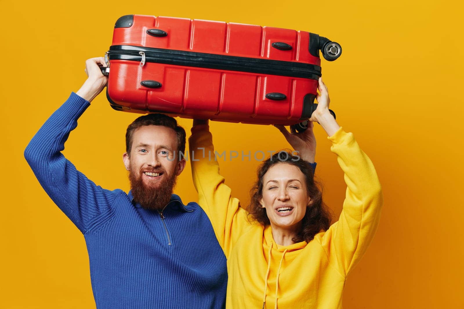 Woman and man smiling, suitcases in hand with yellow and red suitcase smiling merrily and crooked, yellow background, going on a trip, family vacation trip, newlyweds. High quality photo